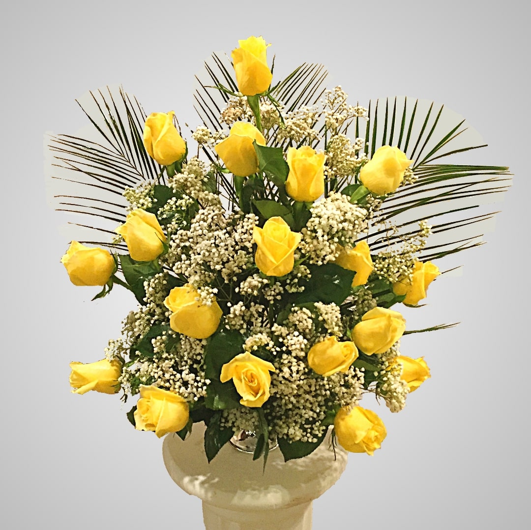 Yellow roses arranged in a vase with white filler flowers and palm fronds