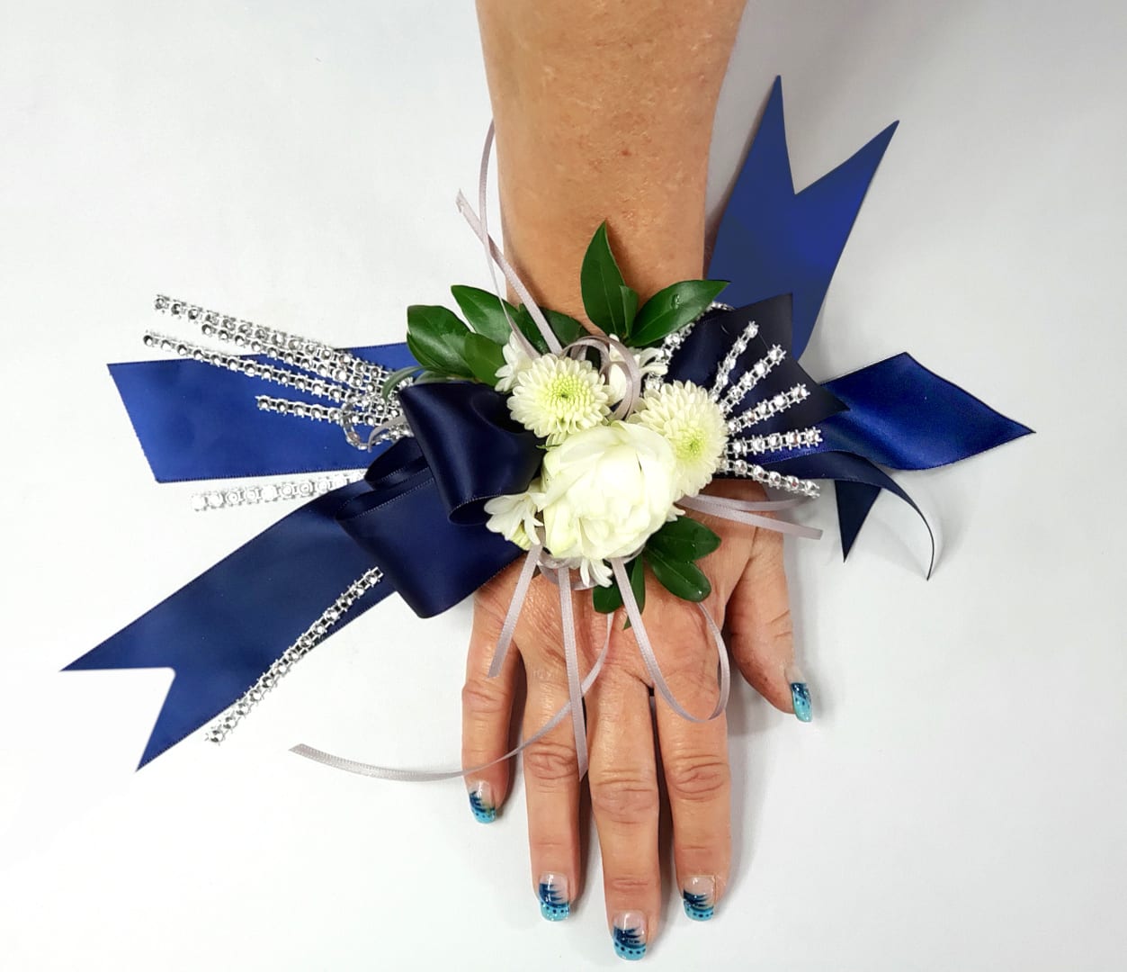 White floral wrist corsage with blue ribbon accents