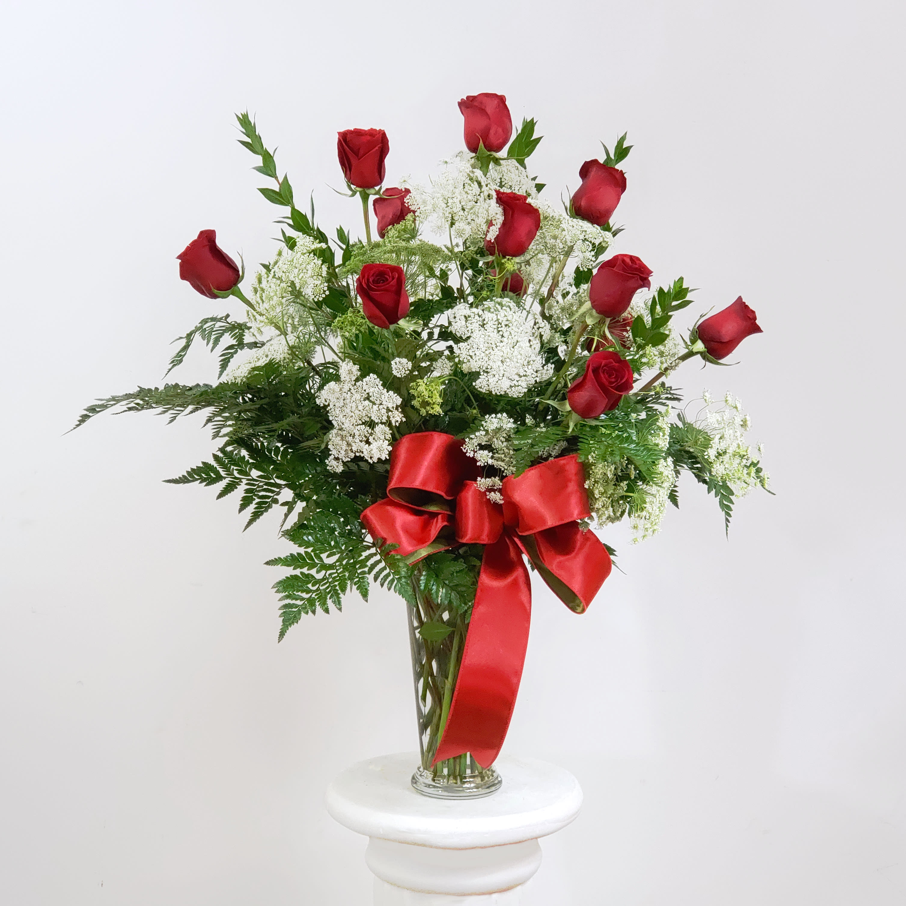 Red roses and white filler flowers in a clear glass vase with a red ribbon