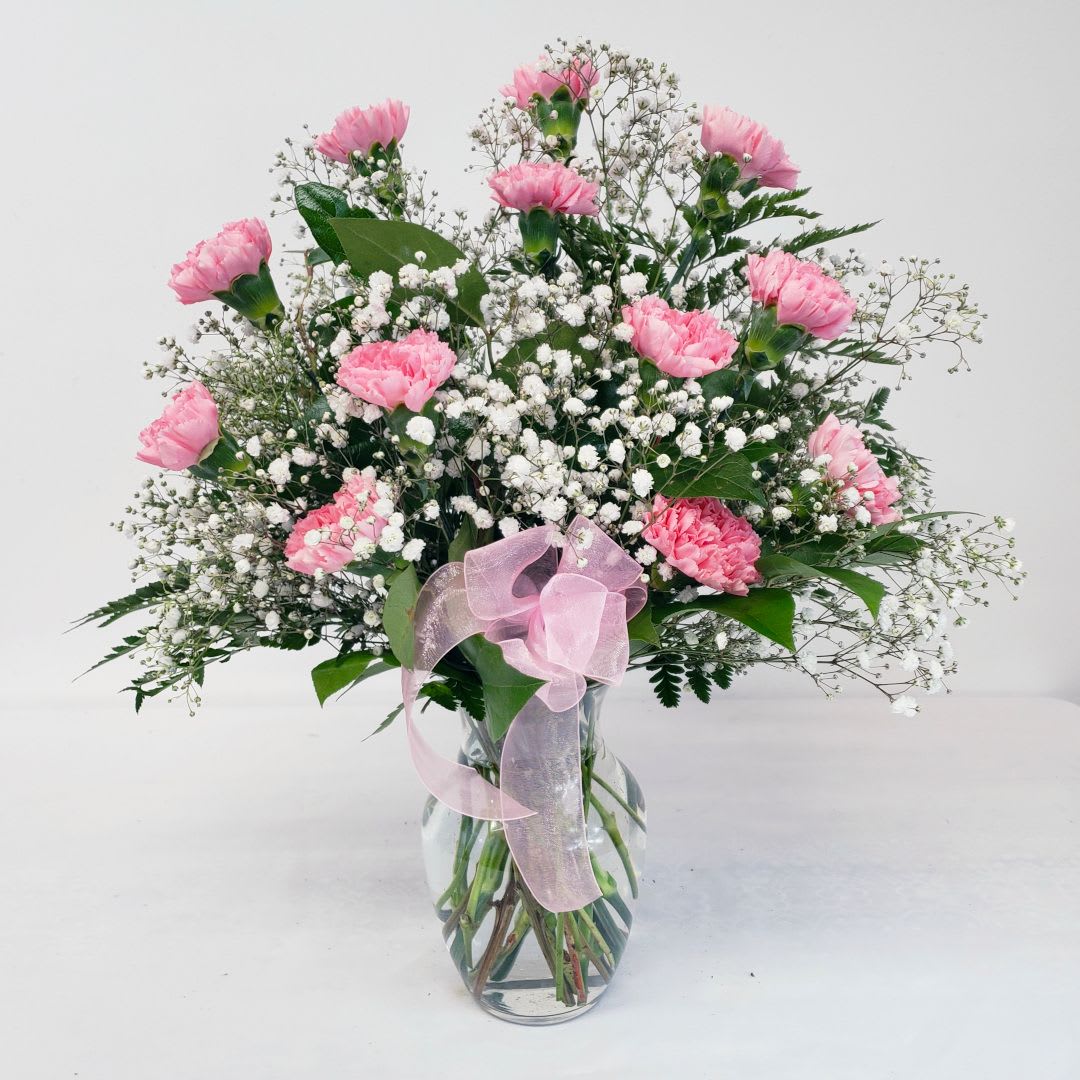 Pink carnations in a glass vase with baby's breath and a pink ribbon