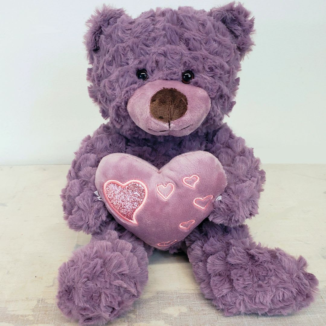 Purple teddy bear holding a pink heart pillow