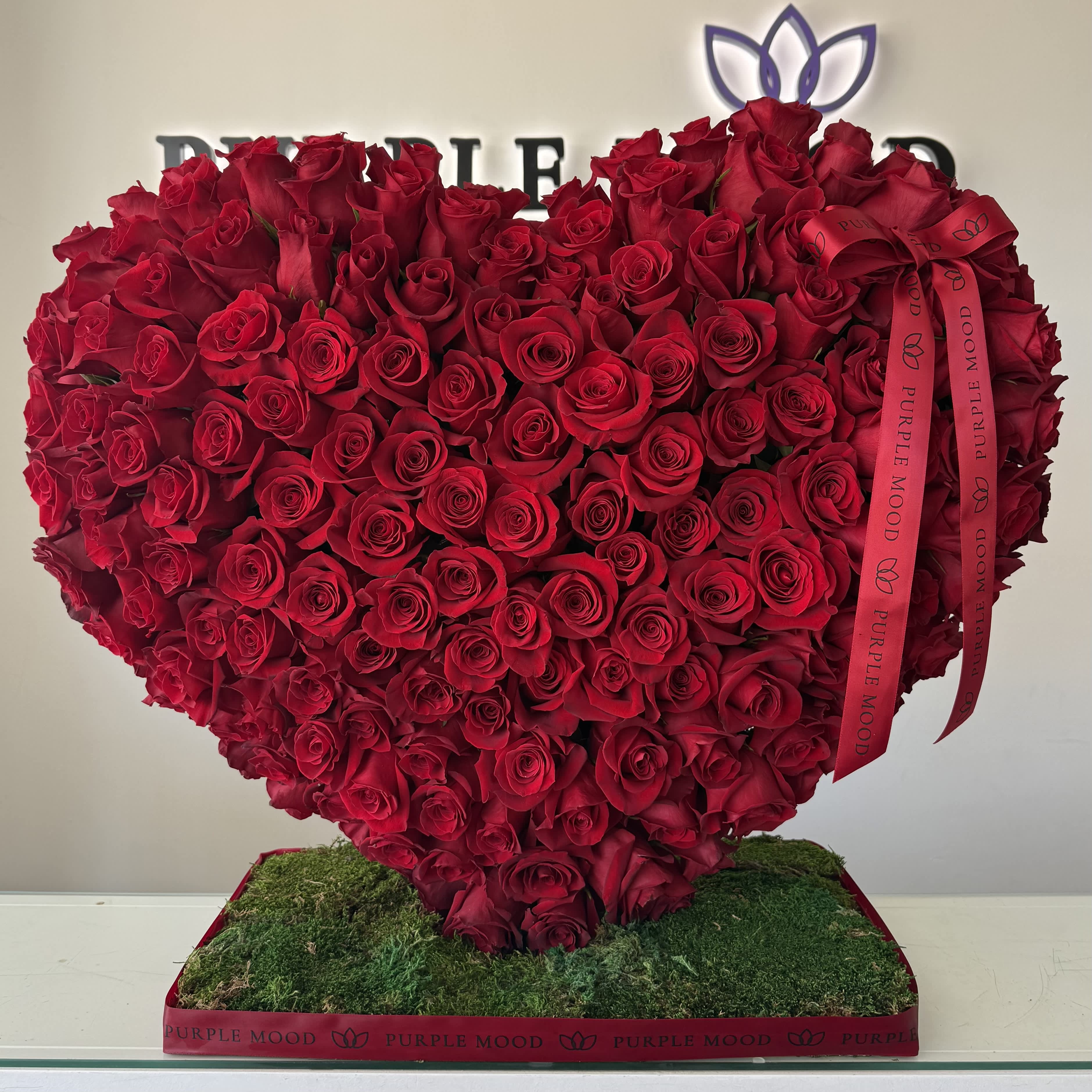Heart-shaped arrangement of red roses on a moss-covered base with a ribbon