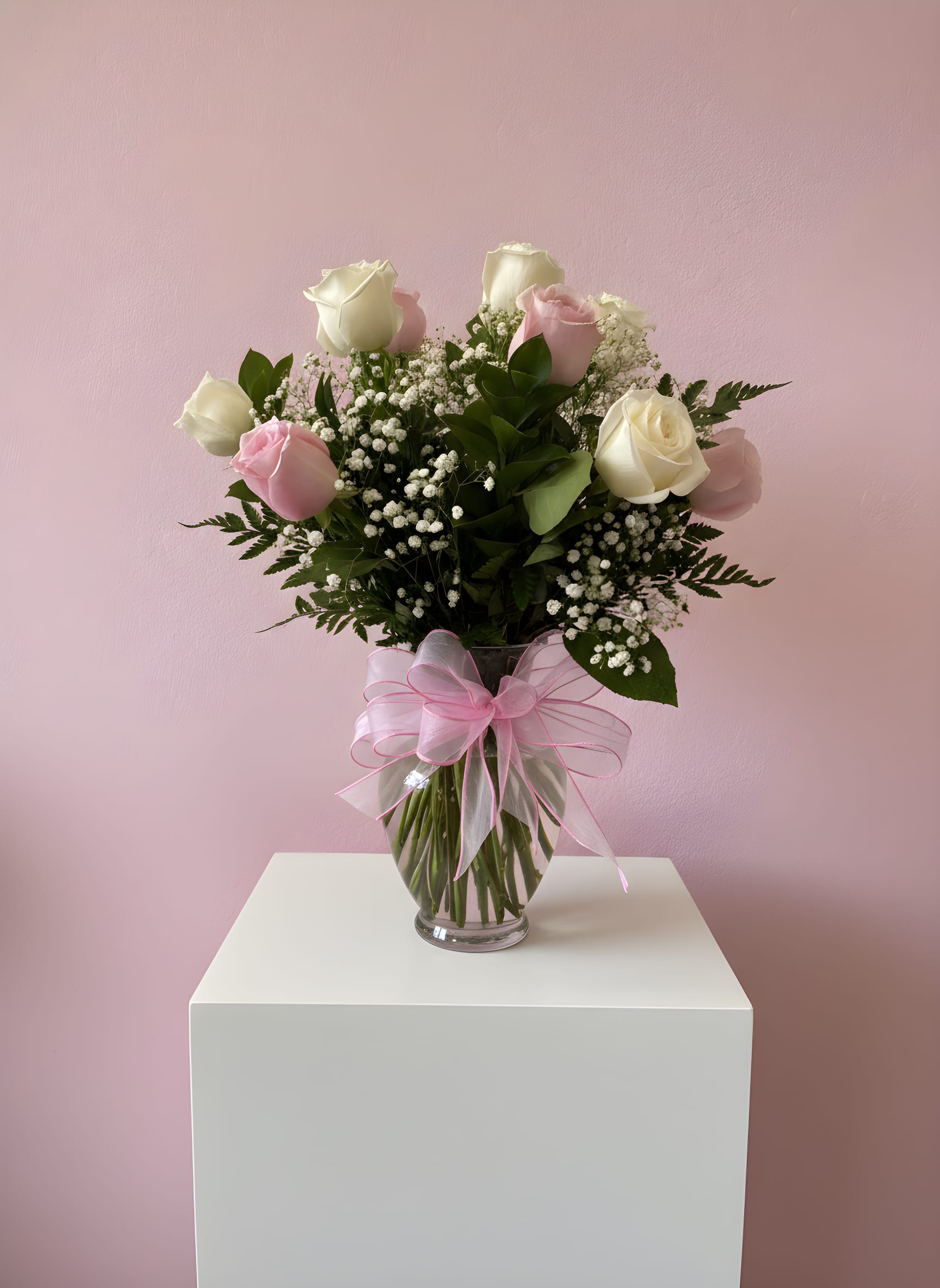 Pink and white roses in a glass vase with a pink ribbon