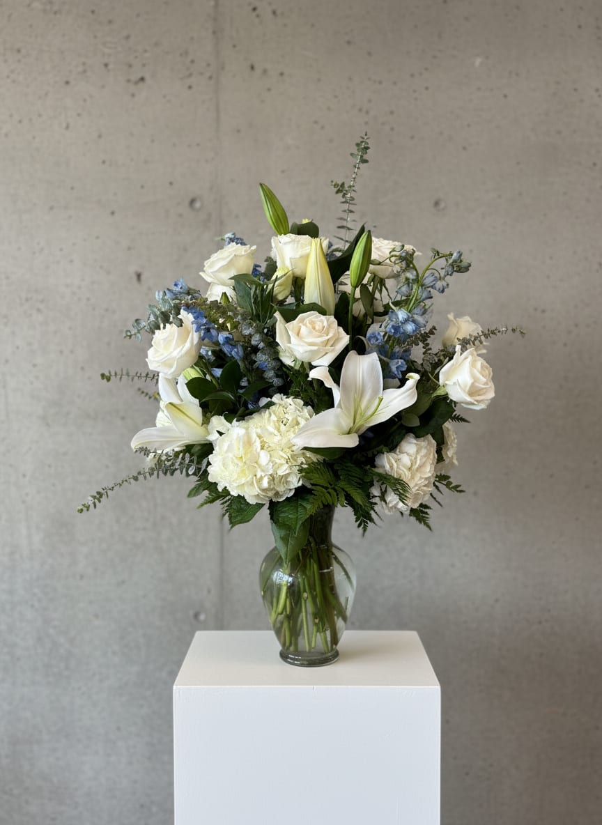 Serene White &amp; Blue Garden Bouquet - Elegant white roses, lilies, and hydrangea mingle with soft blue delphinium and eucalyptus in a classic glass vase. A serene, timeless design perfect for sympathy, weddings, or any occasion calling for quiet elegance.