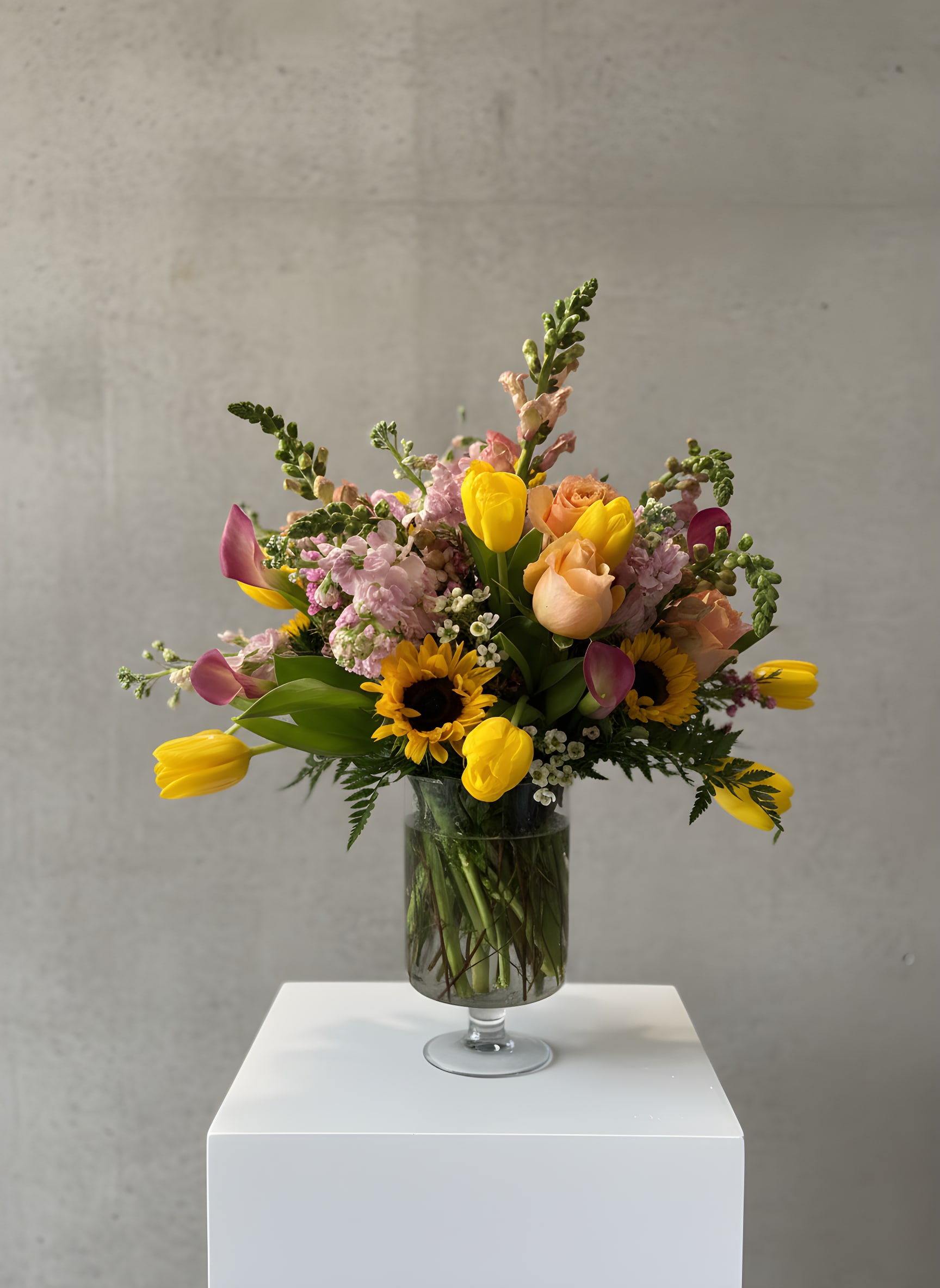 Mixed bouquet of tulips, roses, sunflowers, and pink blooms in a glass vase