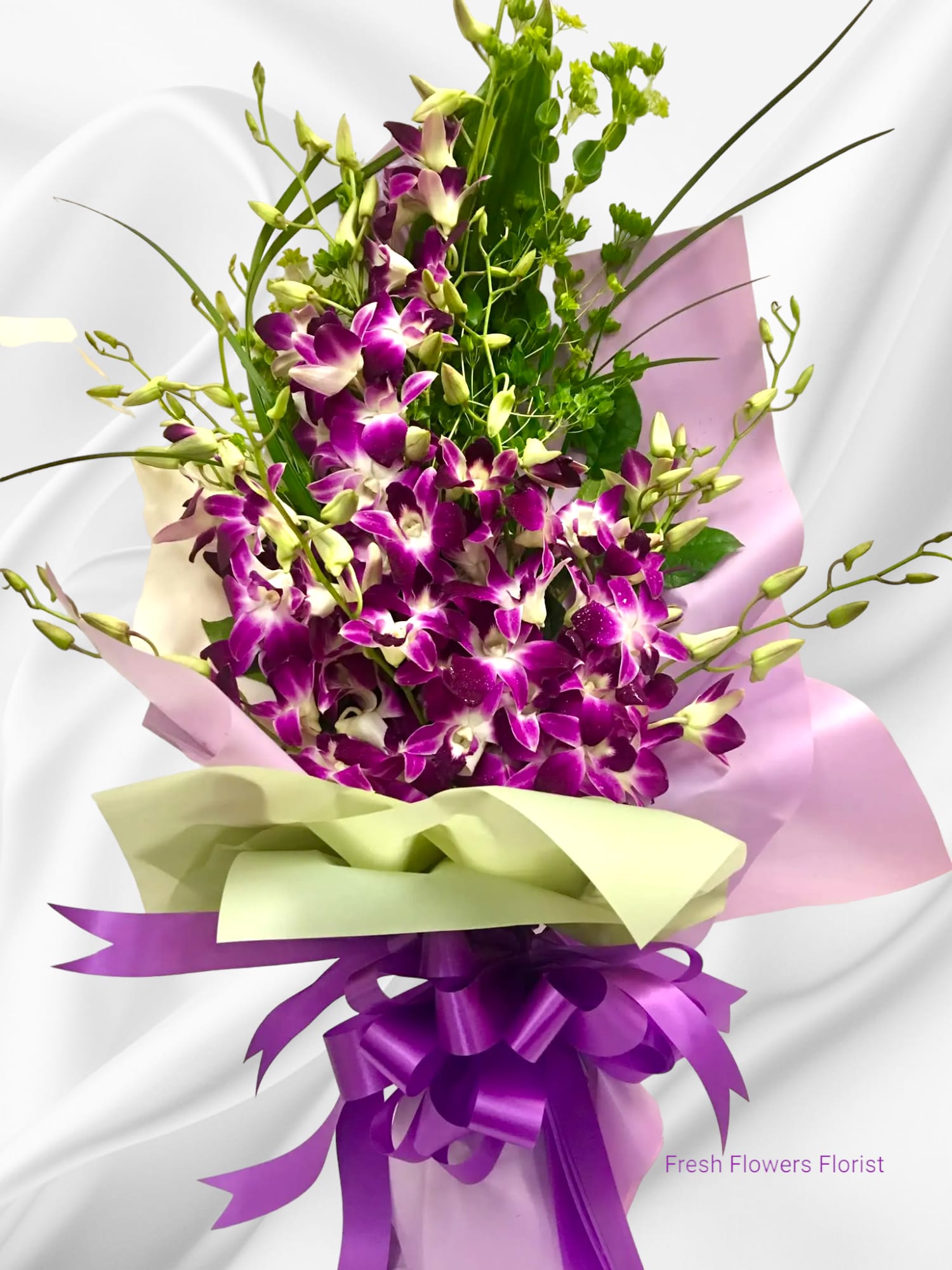 Bouquet of purple orchids wrapped in pink and green paper with a purple ribbon