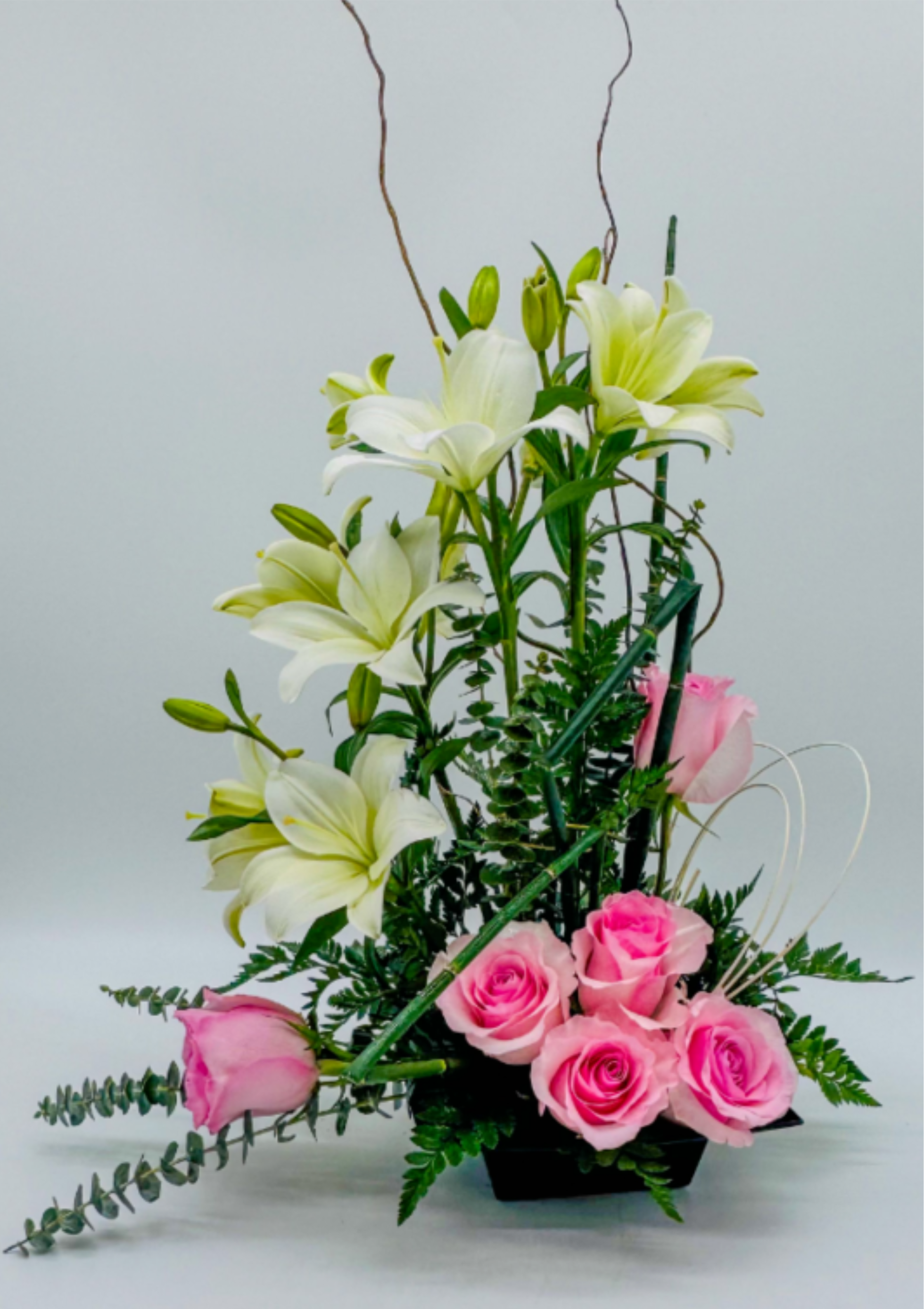 Rose &amp; Lily Cascade - Romantic pink roses cascade downward from a compact base, interwoven with white lilies that rise in graceful height. Lush greenery frames the bouquet, adding texture and depth, while delicate tendrils and curling stems introduce movement. This timeless arrangement exudes elegance and charm, making it perfect gift for the love ones,thatfeel both soft and sophisticated.