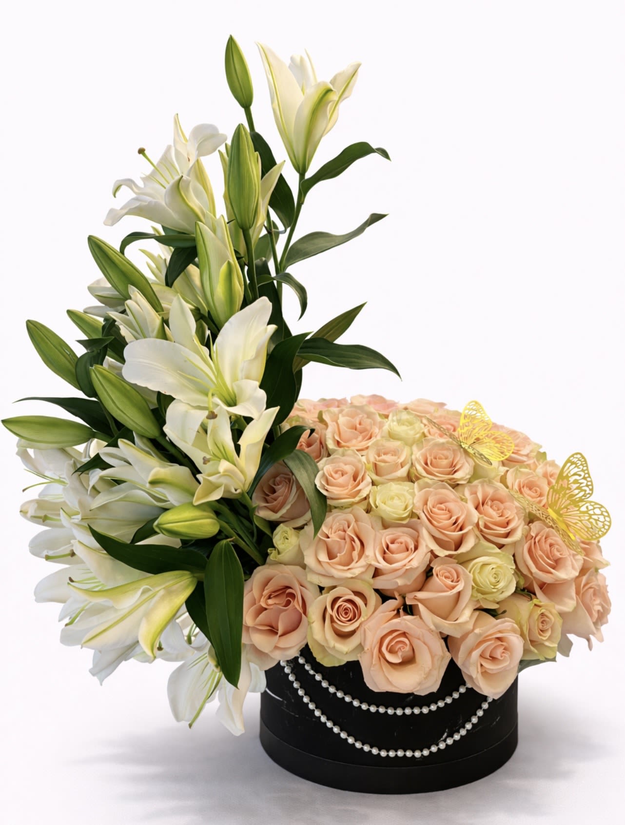 White lilies and peach roses in a black round box with pearl trim