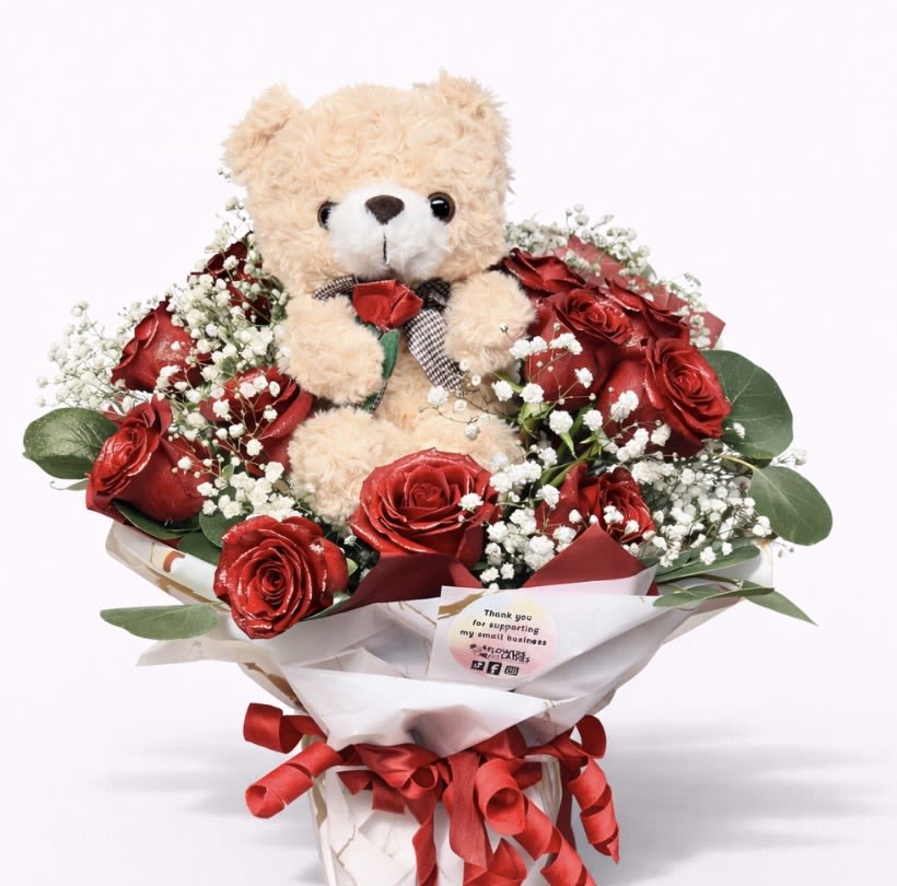Teddy bear surrounded by red roses in a wrapped bouquet