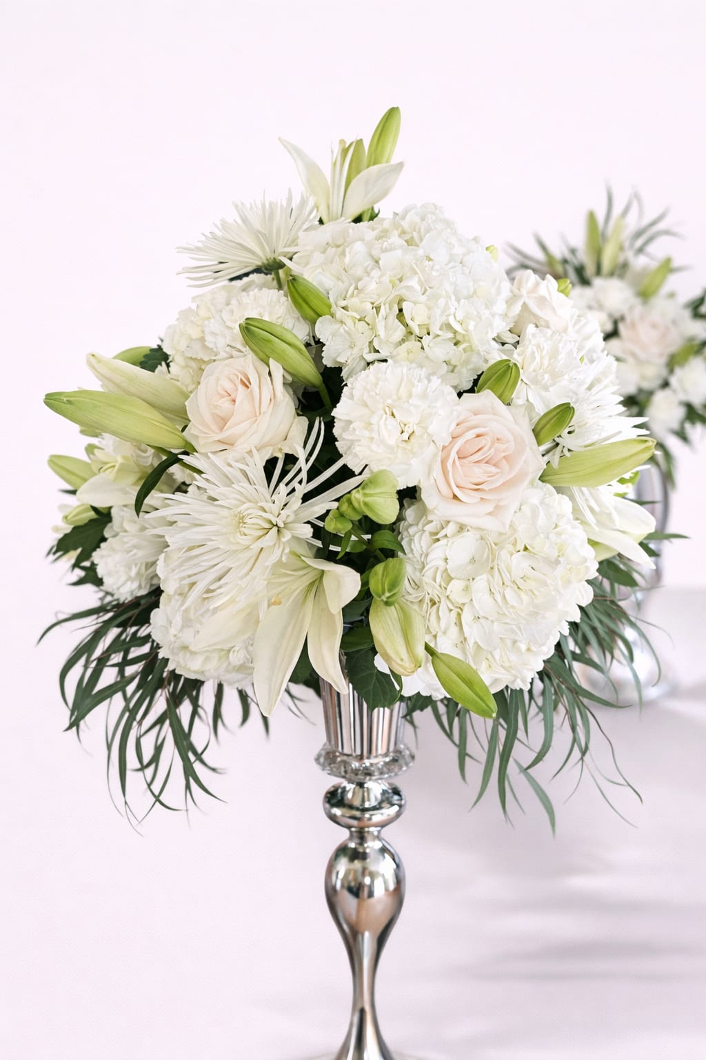 White floral arrangement in a silver vase with lilies and roses