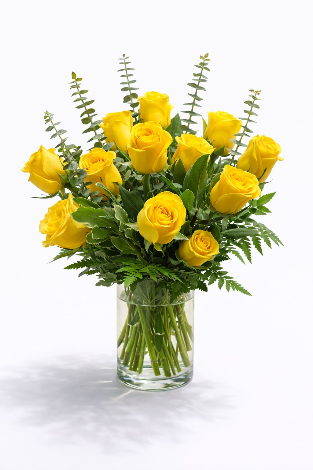 Arrangement of bright yellow roses with greenery in a clear glass vase