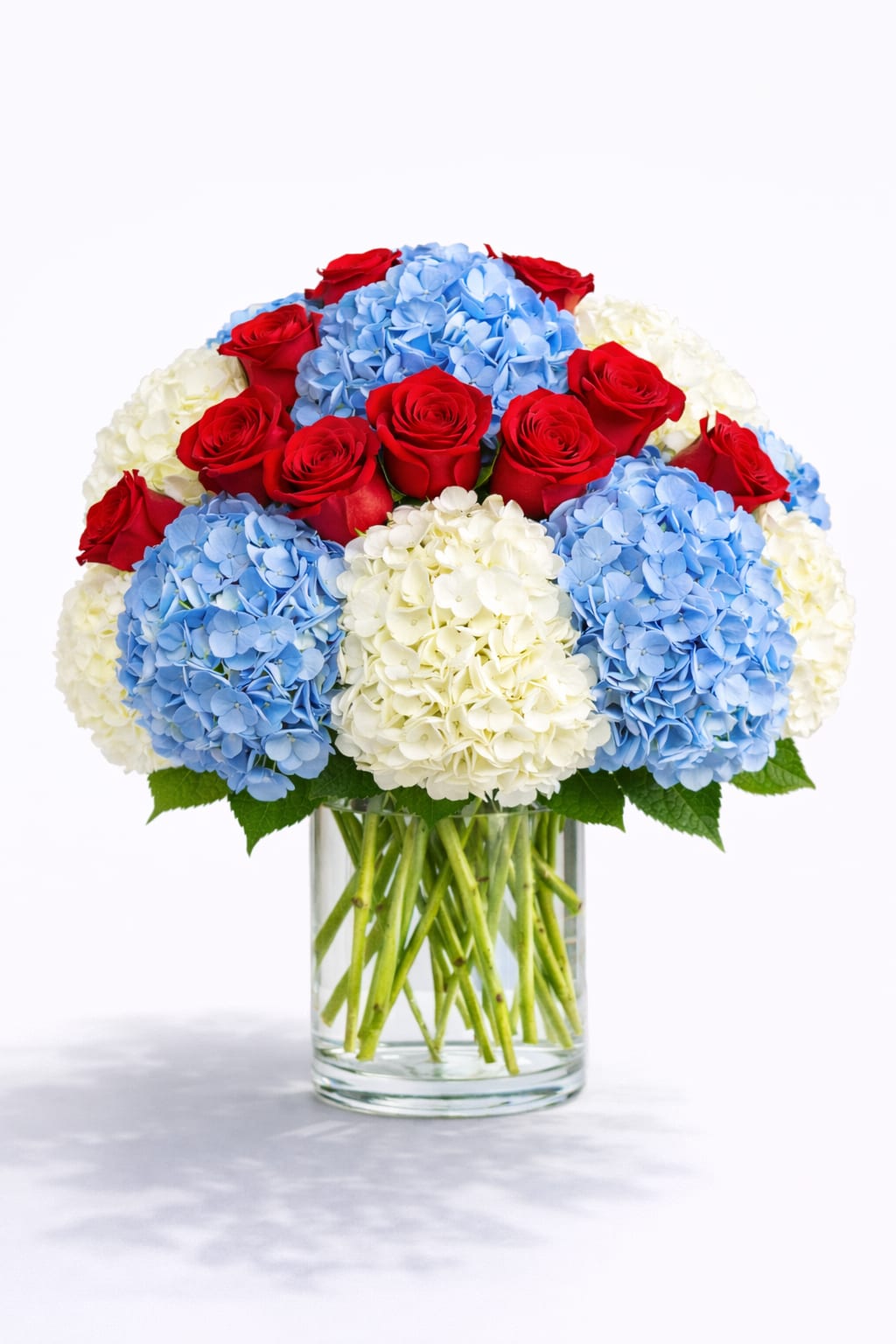Red roses and blue-white hydrangeas in a clear glass vase