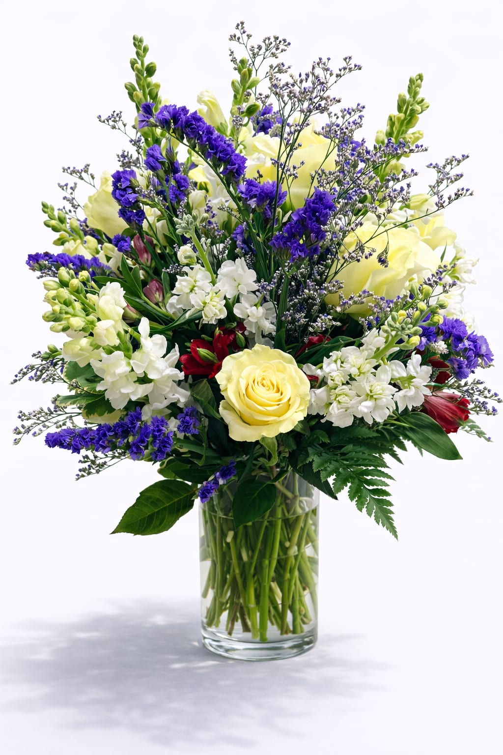 Mixed bouquet of yellow roses, white blooms, and purple flowers in a glass vase