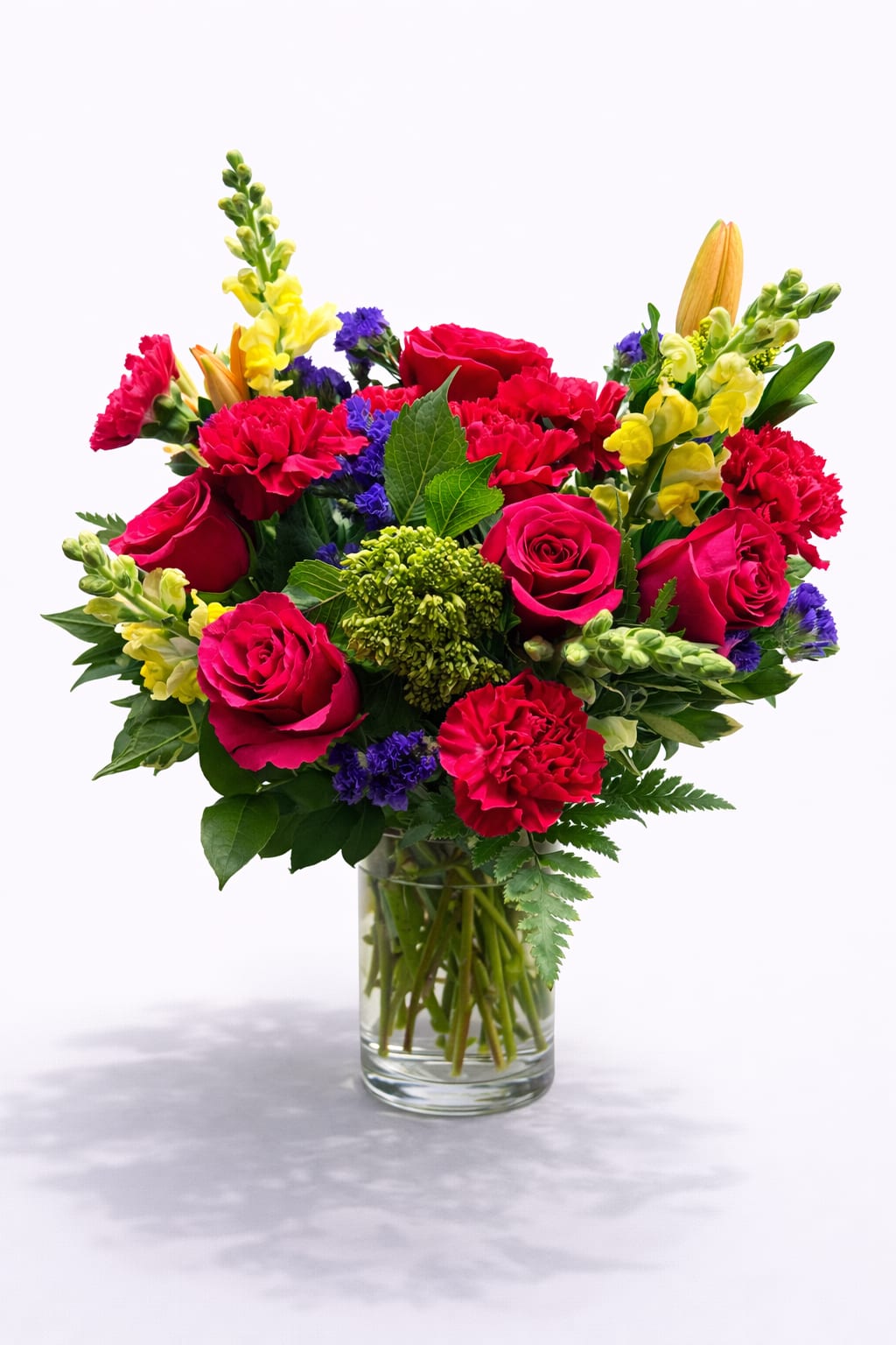 Mixed bouquet of red roses, carnations, and yellow snapdragons in a glass vase