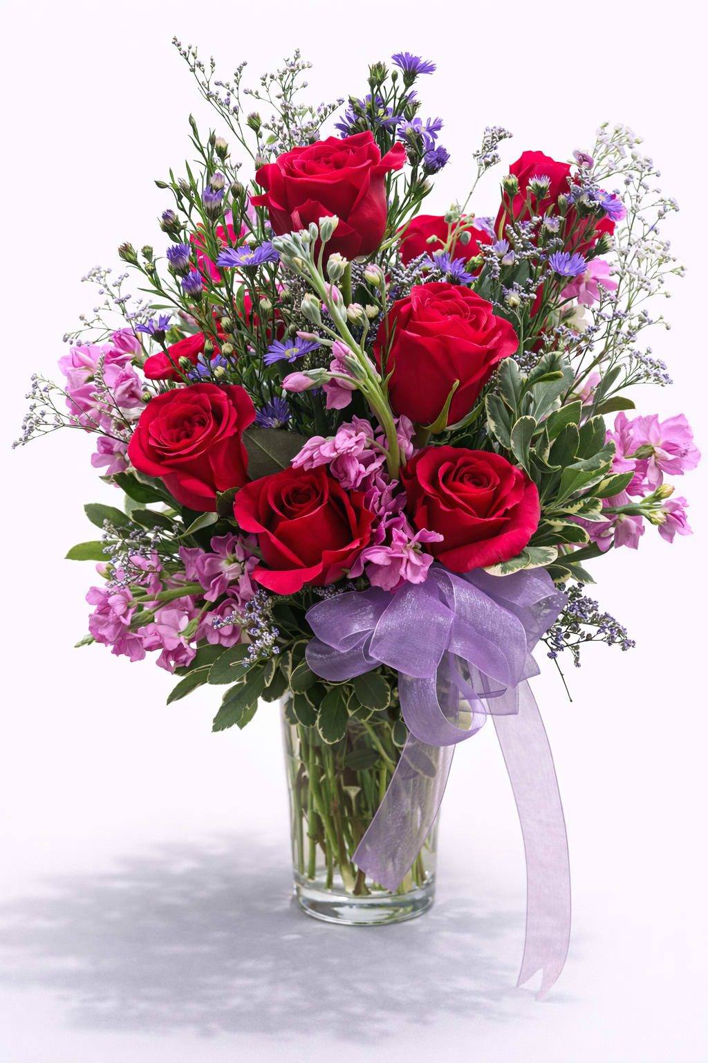 Bouquet of red roses and purple flowers in a glass vase with a lavender ribbon
