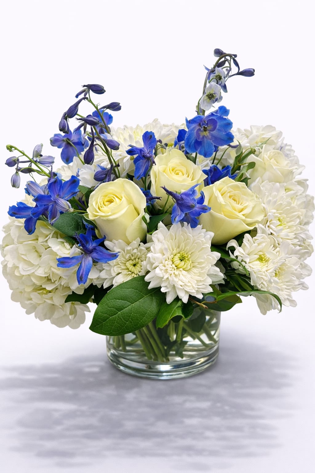 White and pale yellow roses with blue flowers in a glass vase