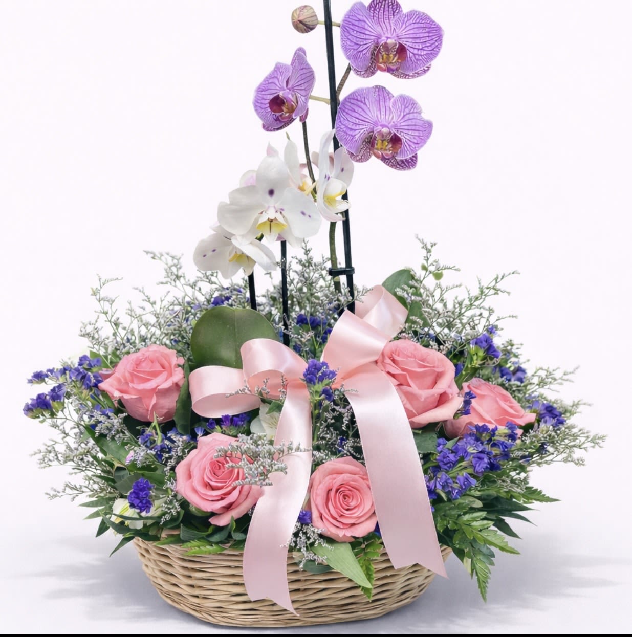 Basket arrangement with pink roses and purple orchids tied with a pink ribbon