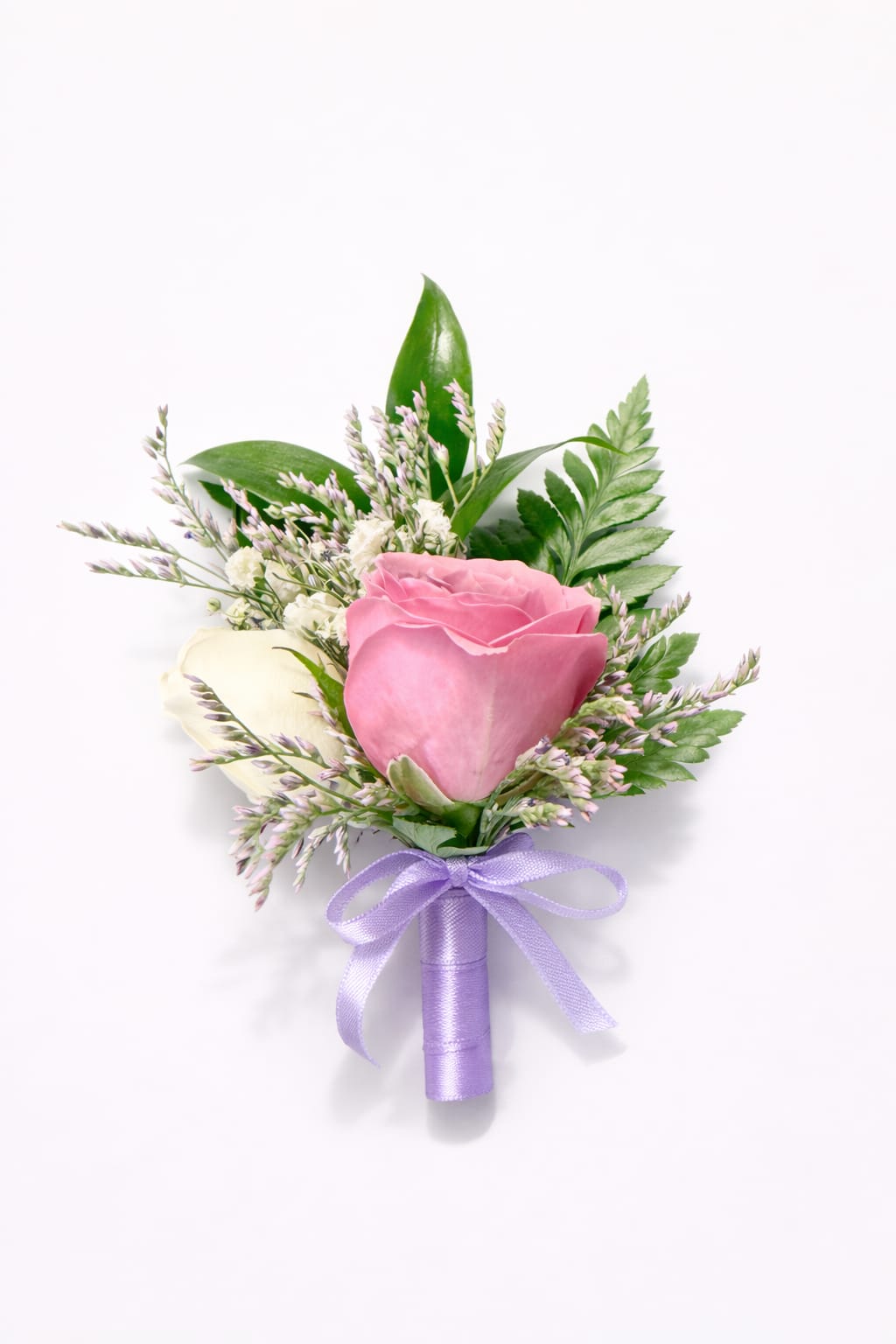 Sweet Romance Boutonniere - Soft, romantic, and beautifully refined, this elegant boutonniere features a delicate pink rose paired with subtle white blooms and fresh greenery. Accented with gentle lavender ribbon and airy filler flowers, it creates a timeless look full of charm and sophistication.  Perfect for weddings, proms, quinceañeras, or any special celebration, this boutonniere adds a graceful and romantic finishing touch that complements both classic and modern styles.  A small detail that makes a beautiful statement.