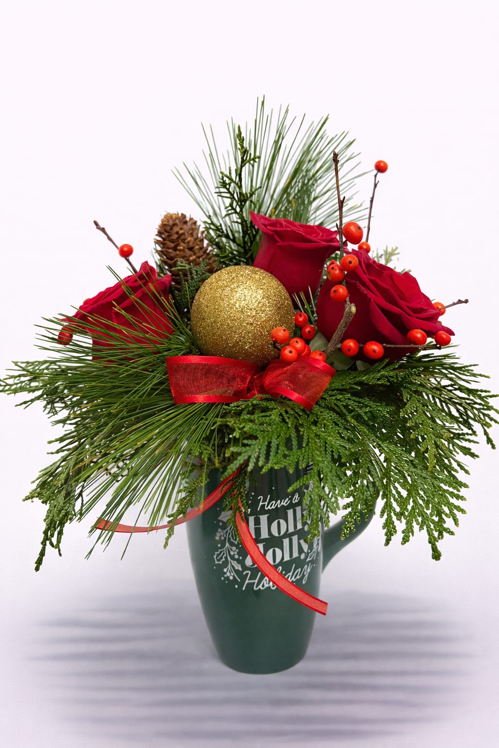 Holiday mug arrangement with red roses, pine branches, berries, and a gold ornament ball