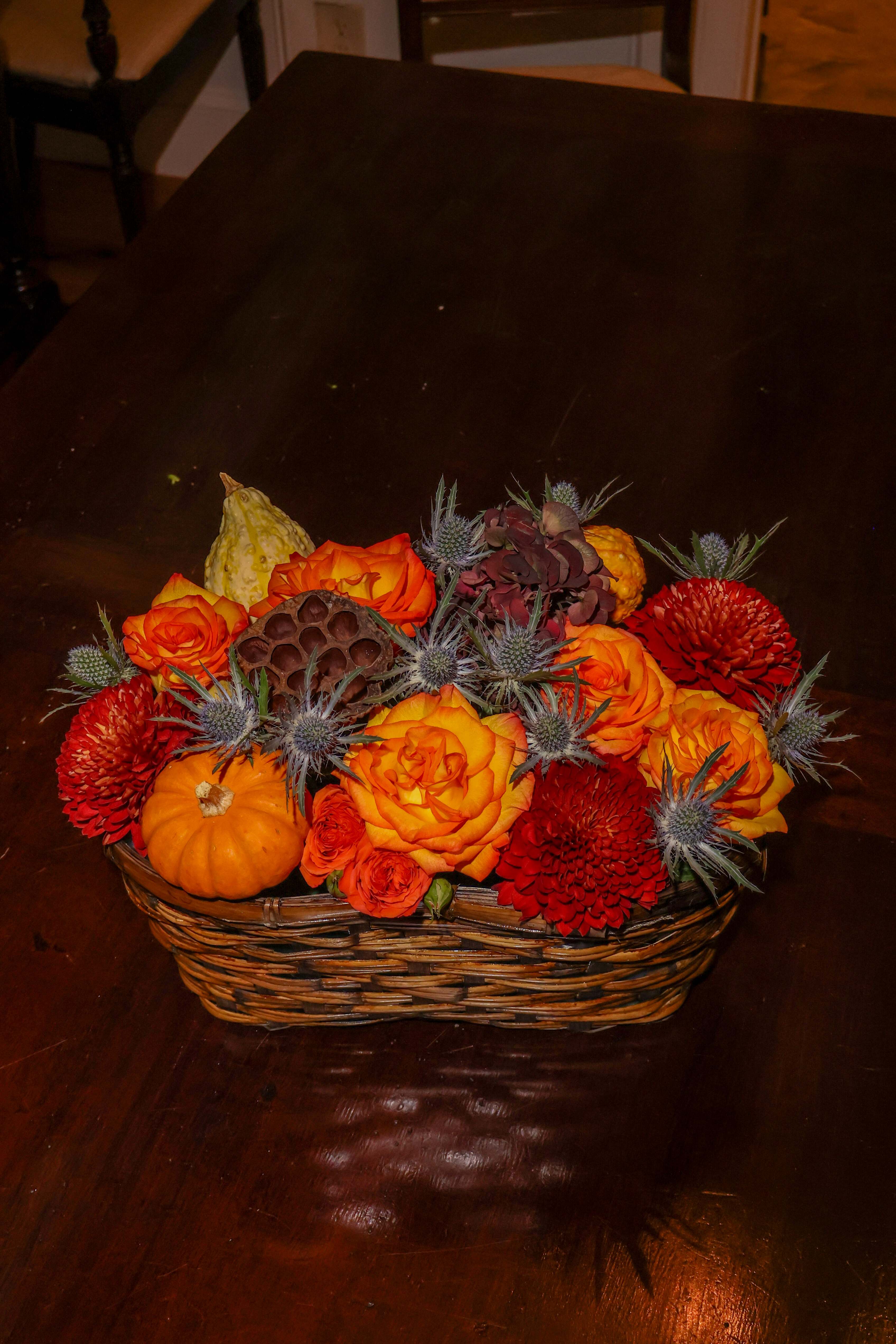 Basket arrangement with orange and red flowers, pumpkins, and thistle-like accents