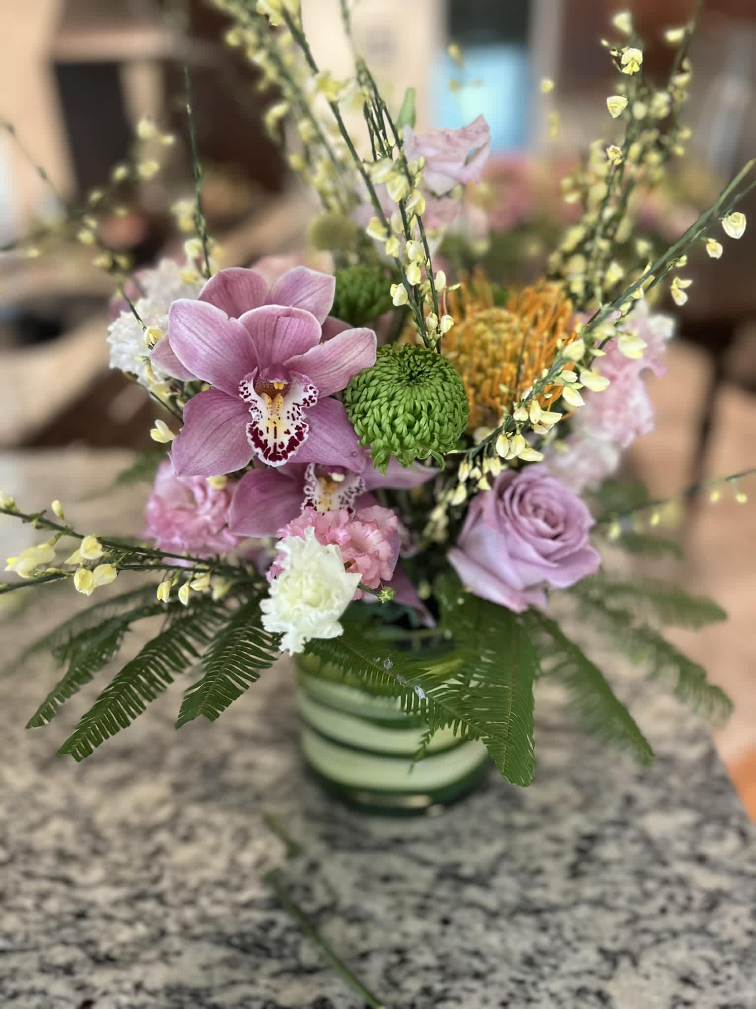 Pink orchids and roses in a striped vase with green accents