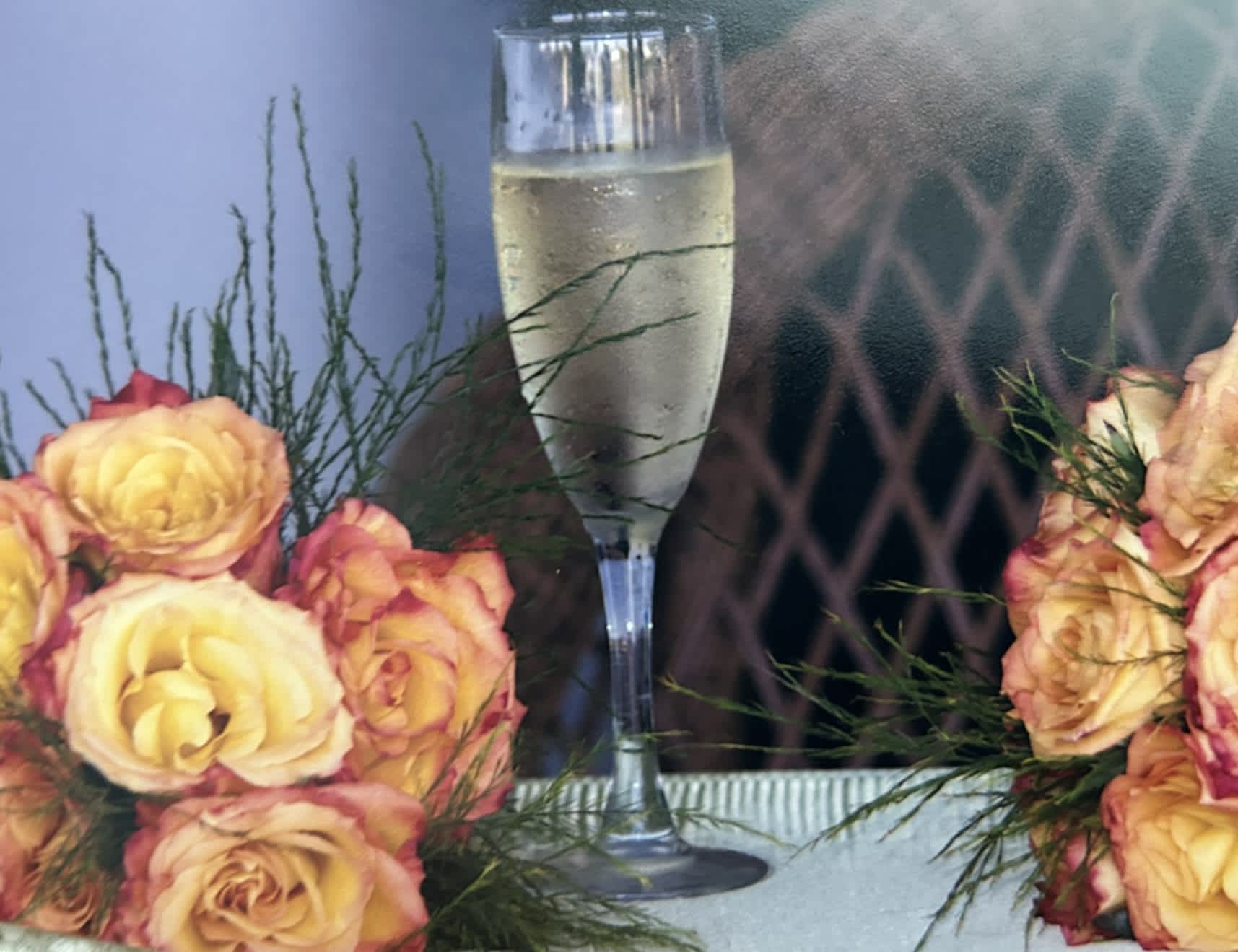 Yellow and pink roses arranged beside a champagne flute