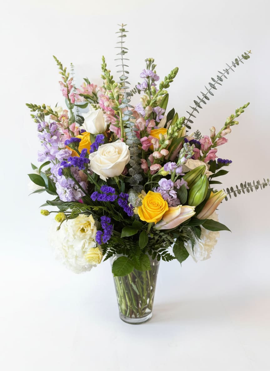 Wildflower Garden Mix - White and yellow roses join lavender stock, purple statice, pink snapdragons, and lily buds in a lush, garden-style mix with white hydrangea and eucalyptus. Full of color and natural, wildflower charm.