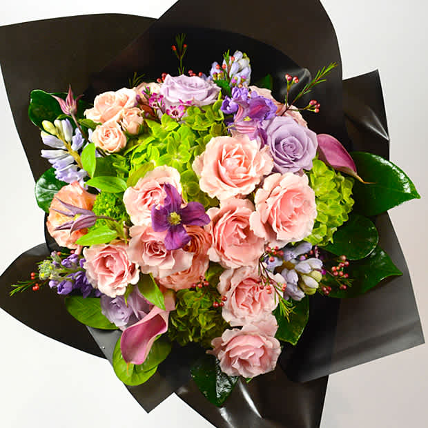 Bouquet of pink and lavender roses with green hydrangeas in black wrap