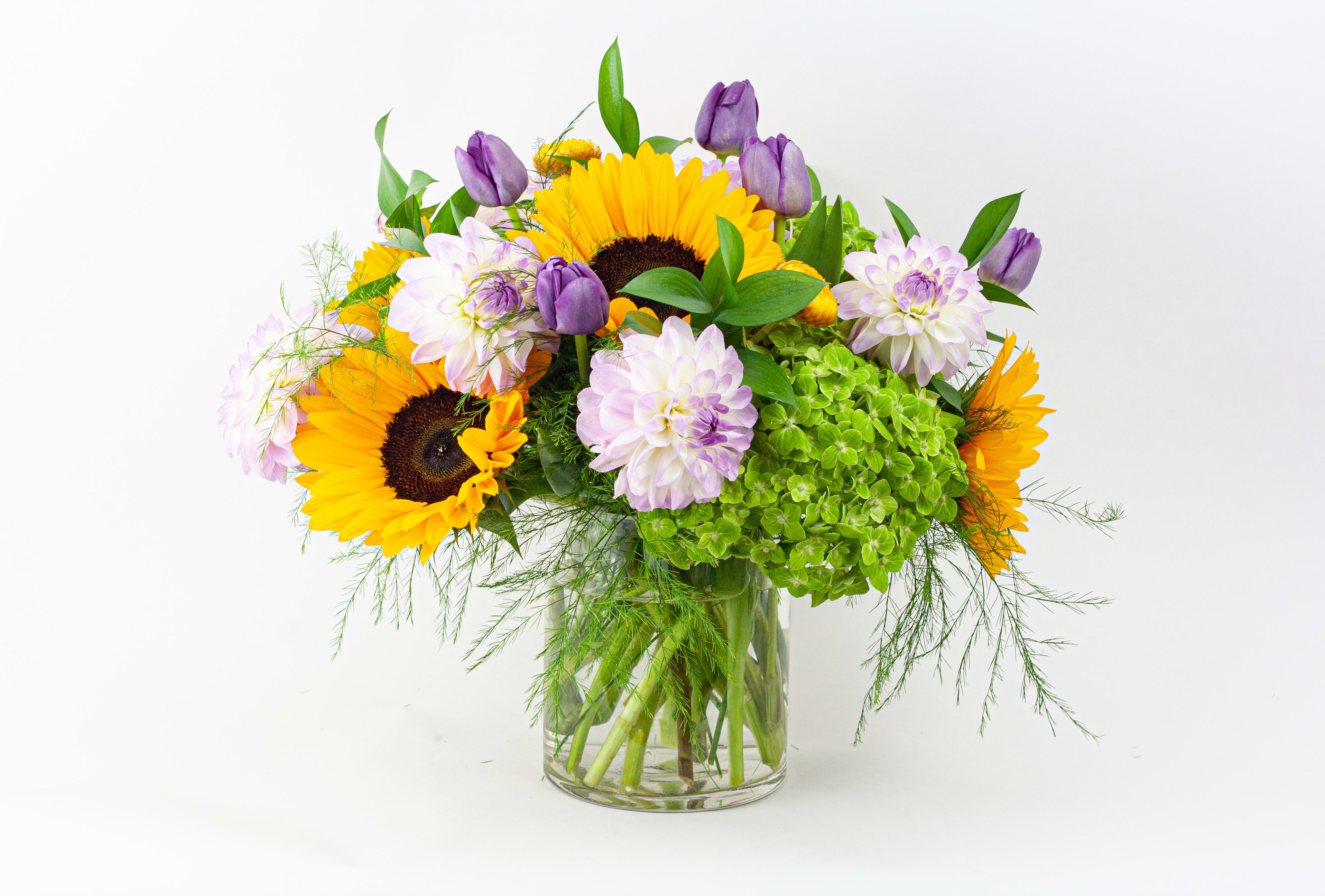Sunflowers and purple blooms in a clear glass vase