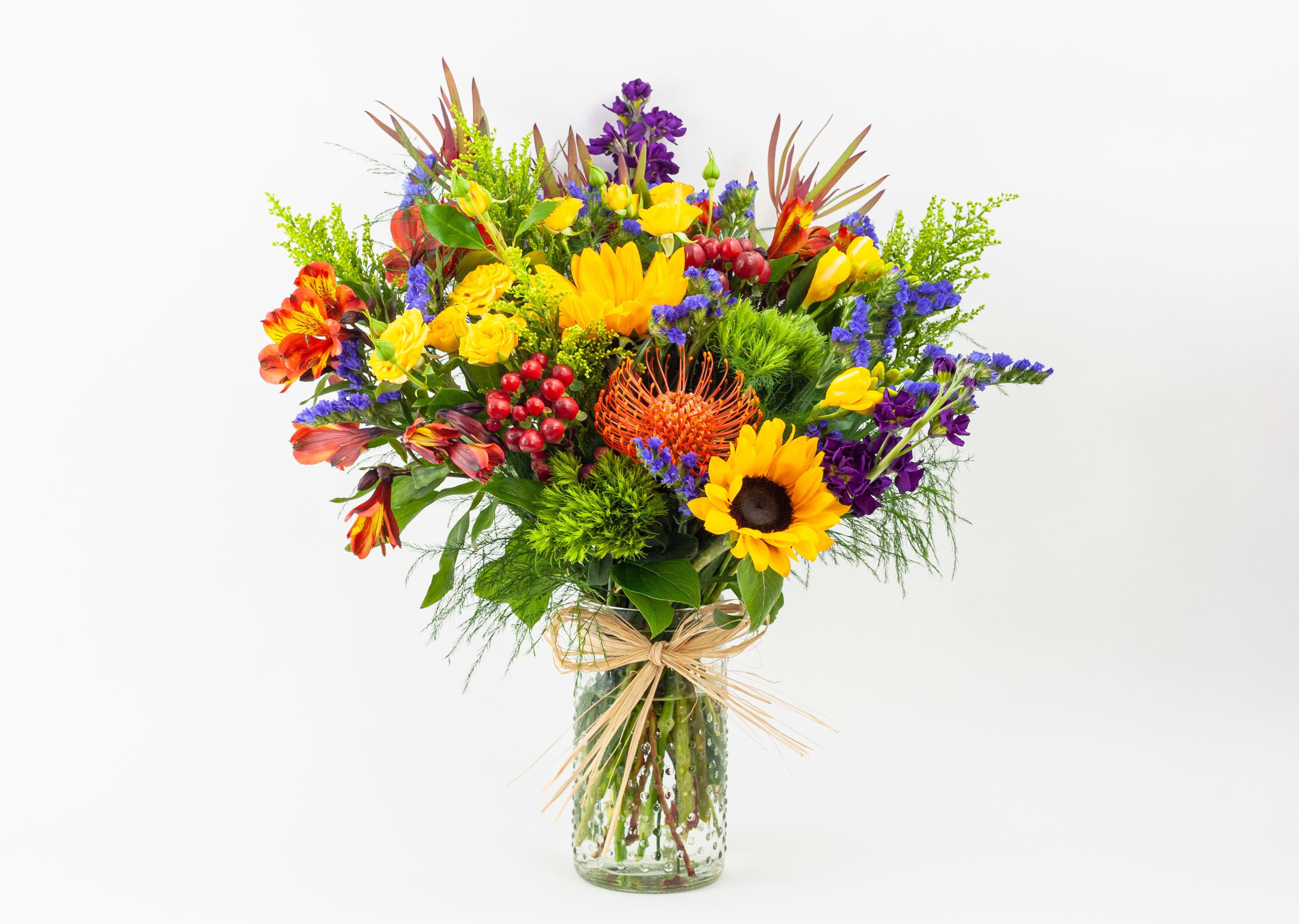 Bright mixed bouquet in a clear glass vase with a raffia bow