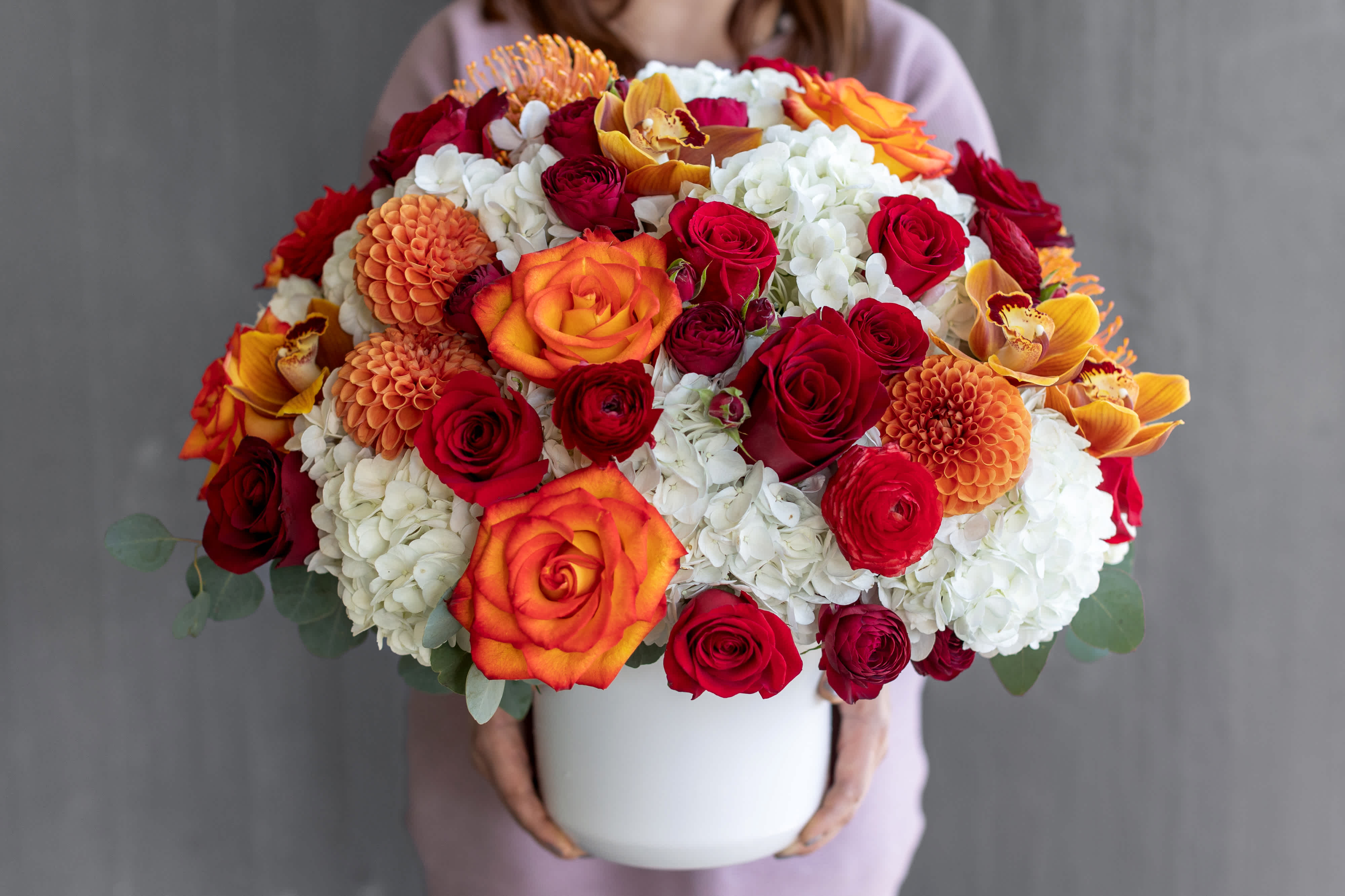 Large bouquet of red, orange, and white flowers in a white vase
