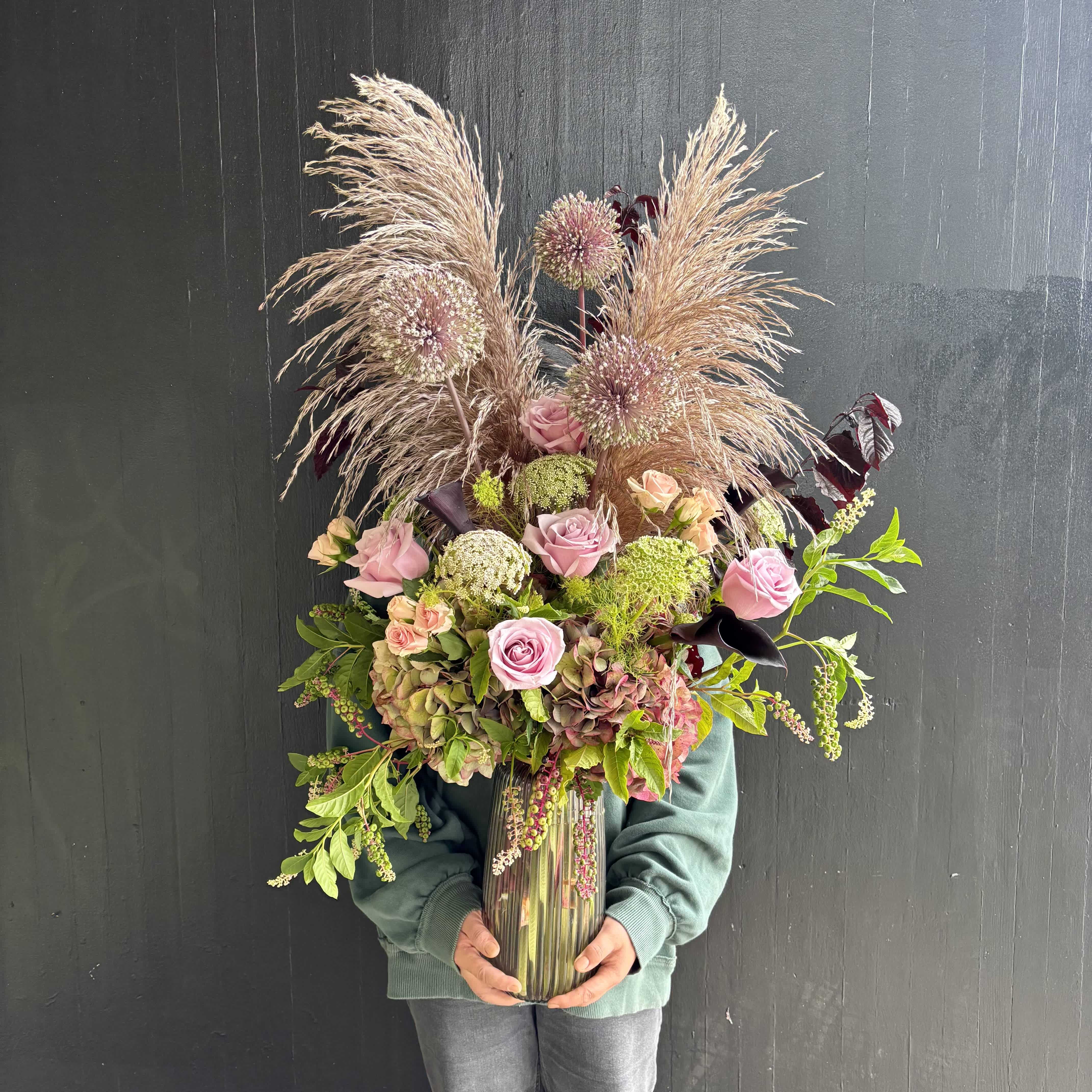 Tall bouquet of pink roses and dried grasses in a glass vase