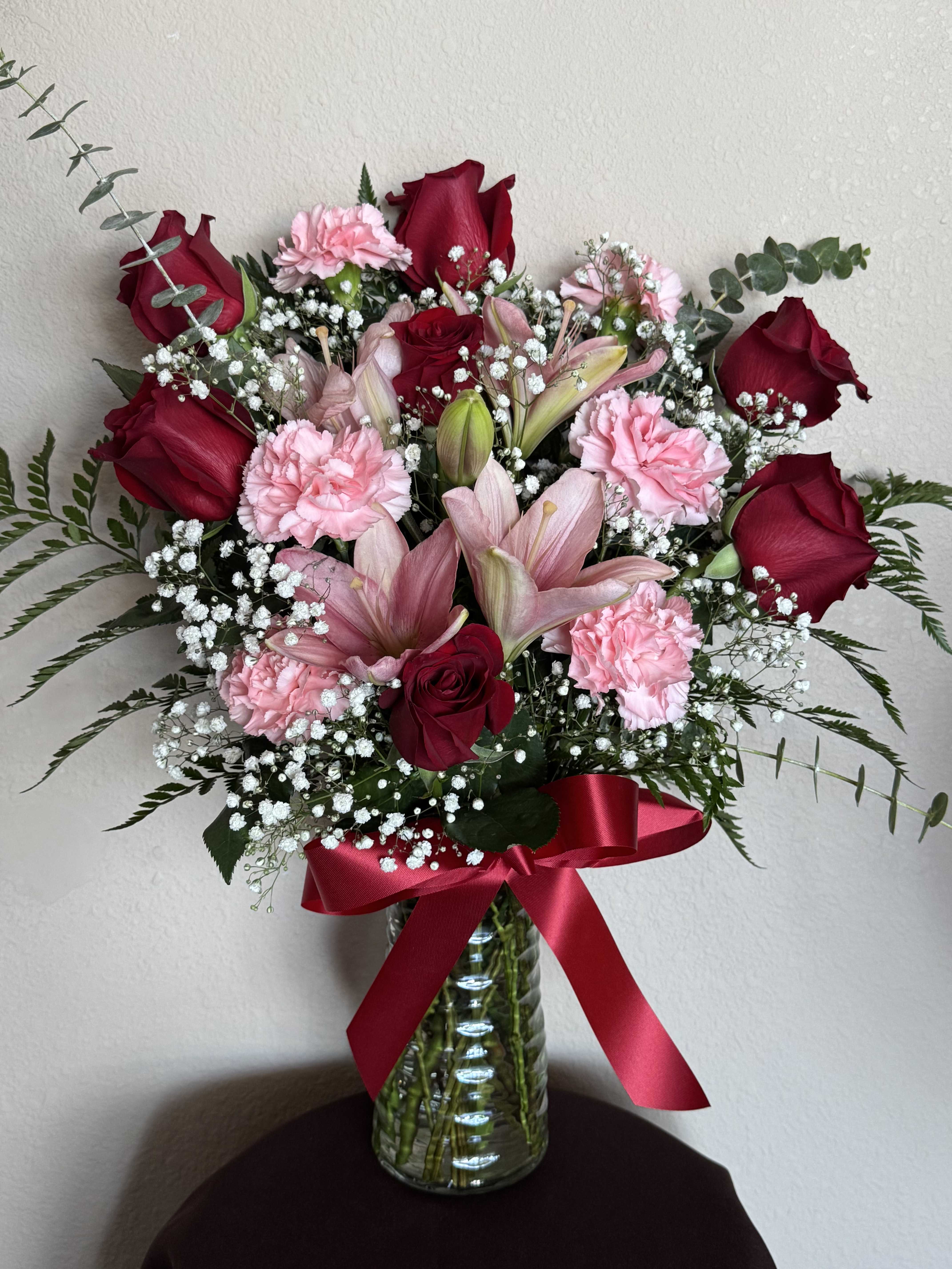 Bouquet of red roses and pink carnations in a glass vase with a red ribbon