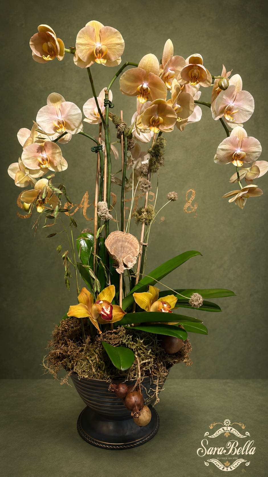Tall orchid arrangement in a dark pedestal vase with moss and decorative accents