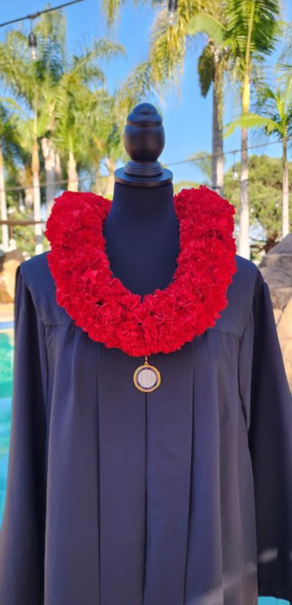 Red floral lei draped over a dark graduation gown