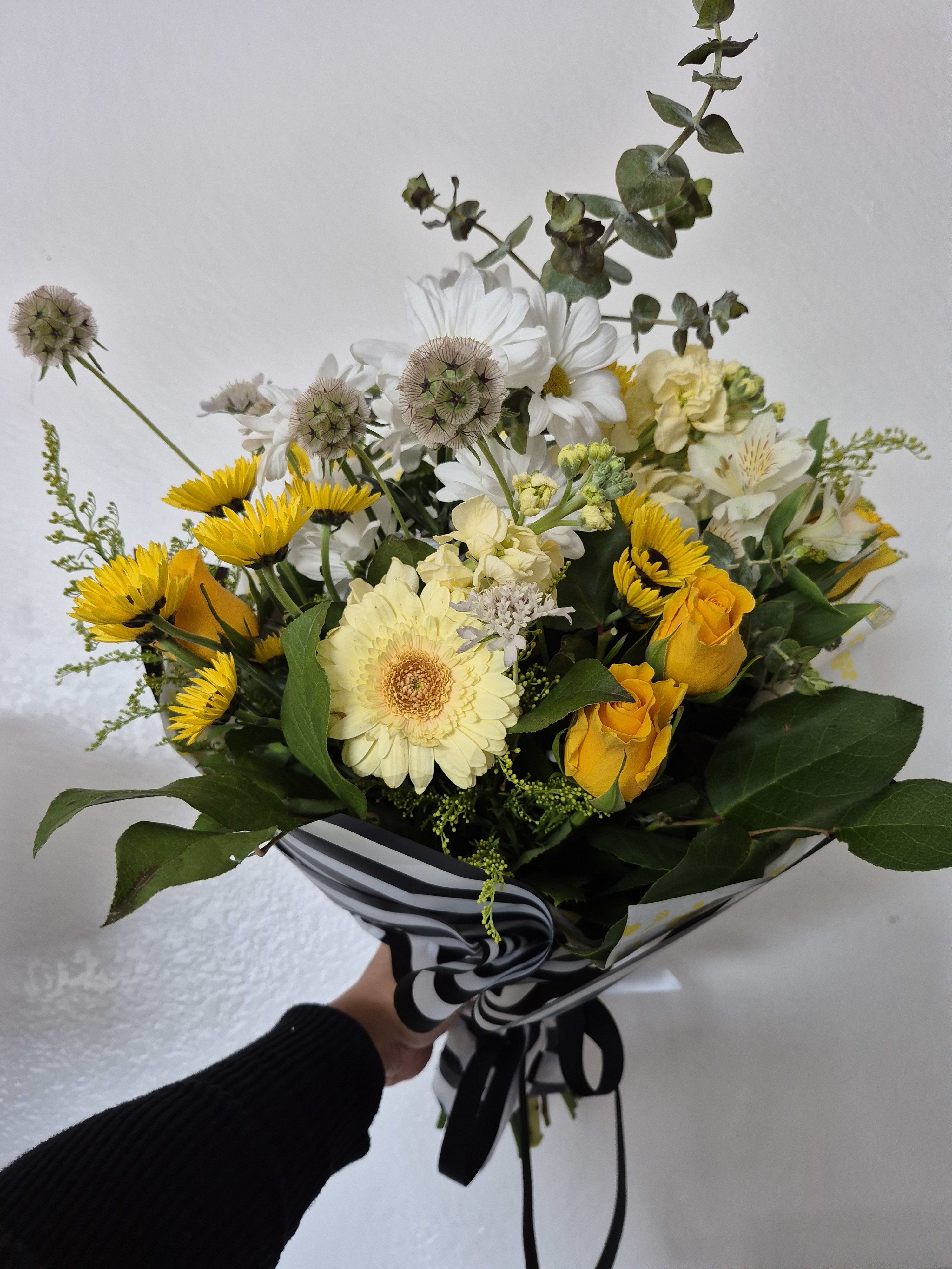 Bouquet of yellow roses, white daisies, and pale blooms wrapped in striped paper