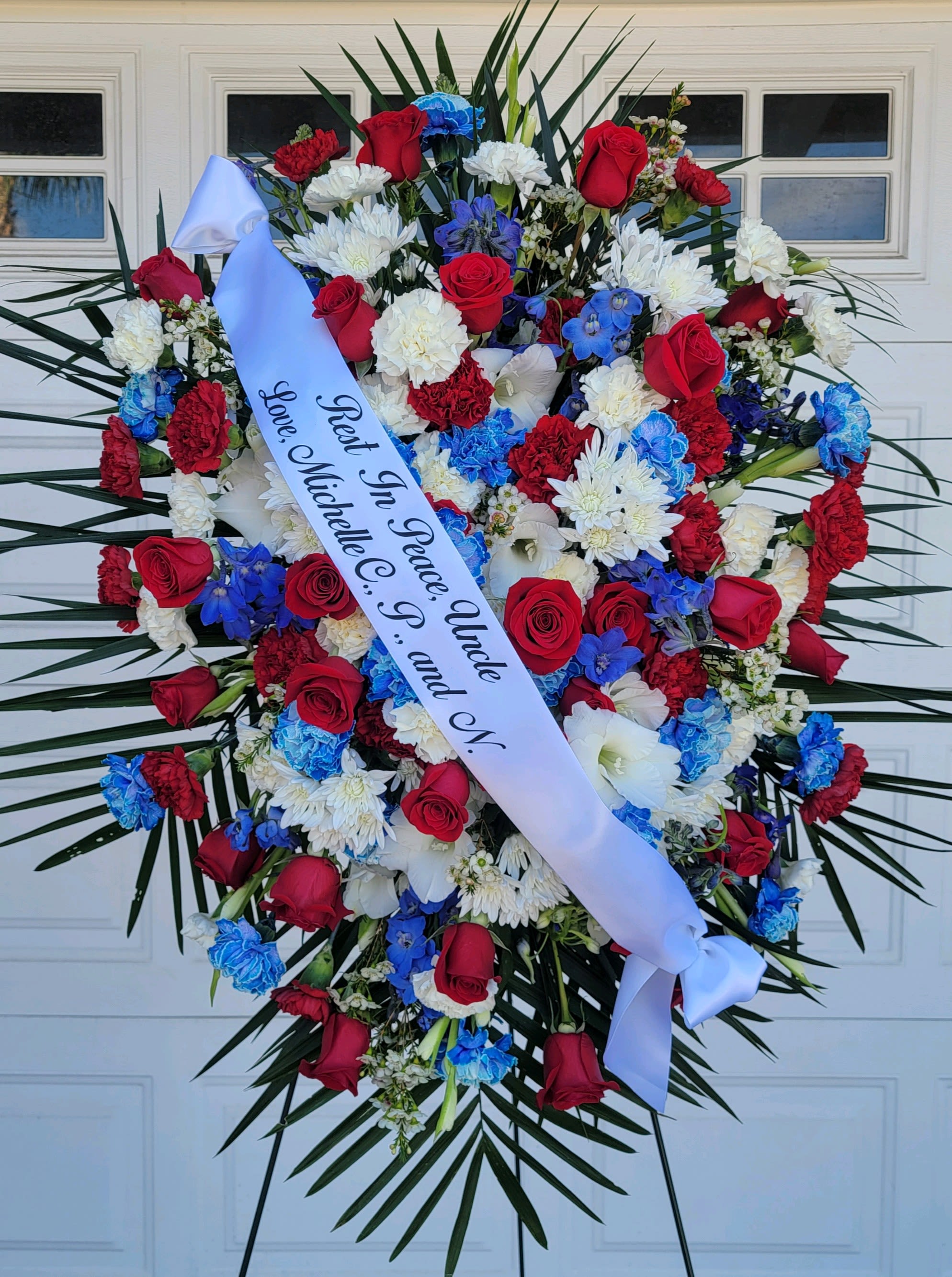 Large funeral wreath of red, white, and blue flowers with a memorial ribbon