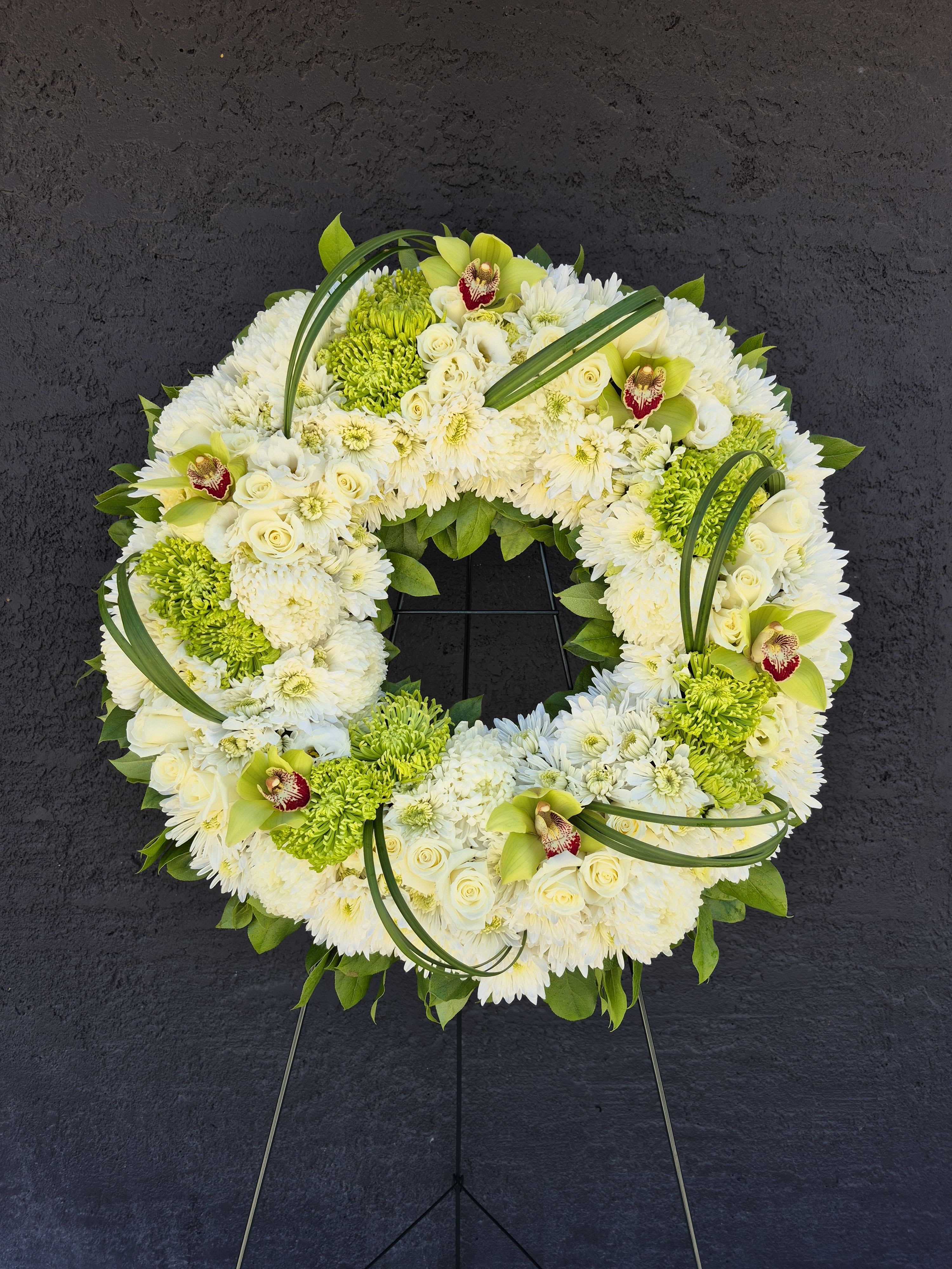 White and green floral wreath on a stand with orchids and chrysanthemums
