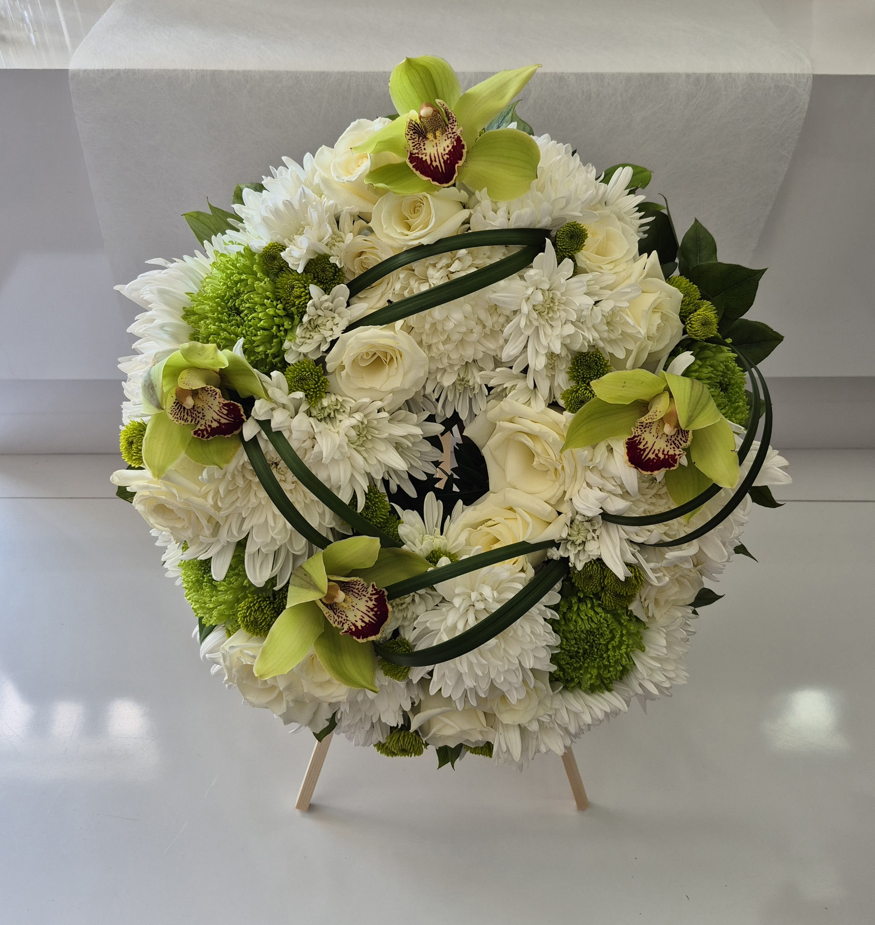 Round white floral arrangement with green orchids and roses on a stand