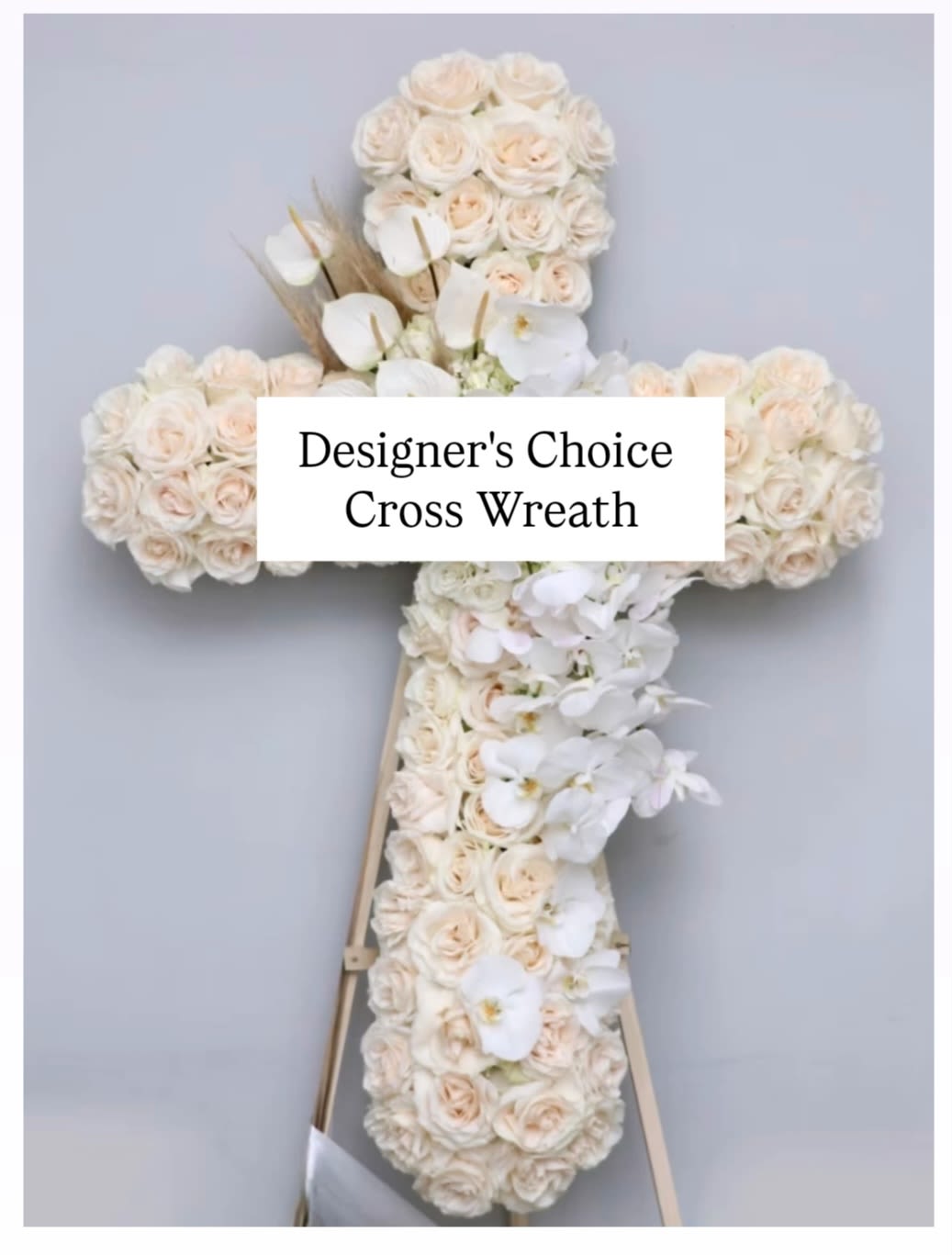 White floral cross wreath on a stand with pale roses and orchids