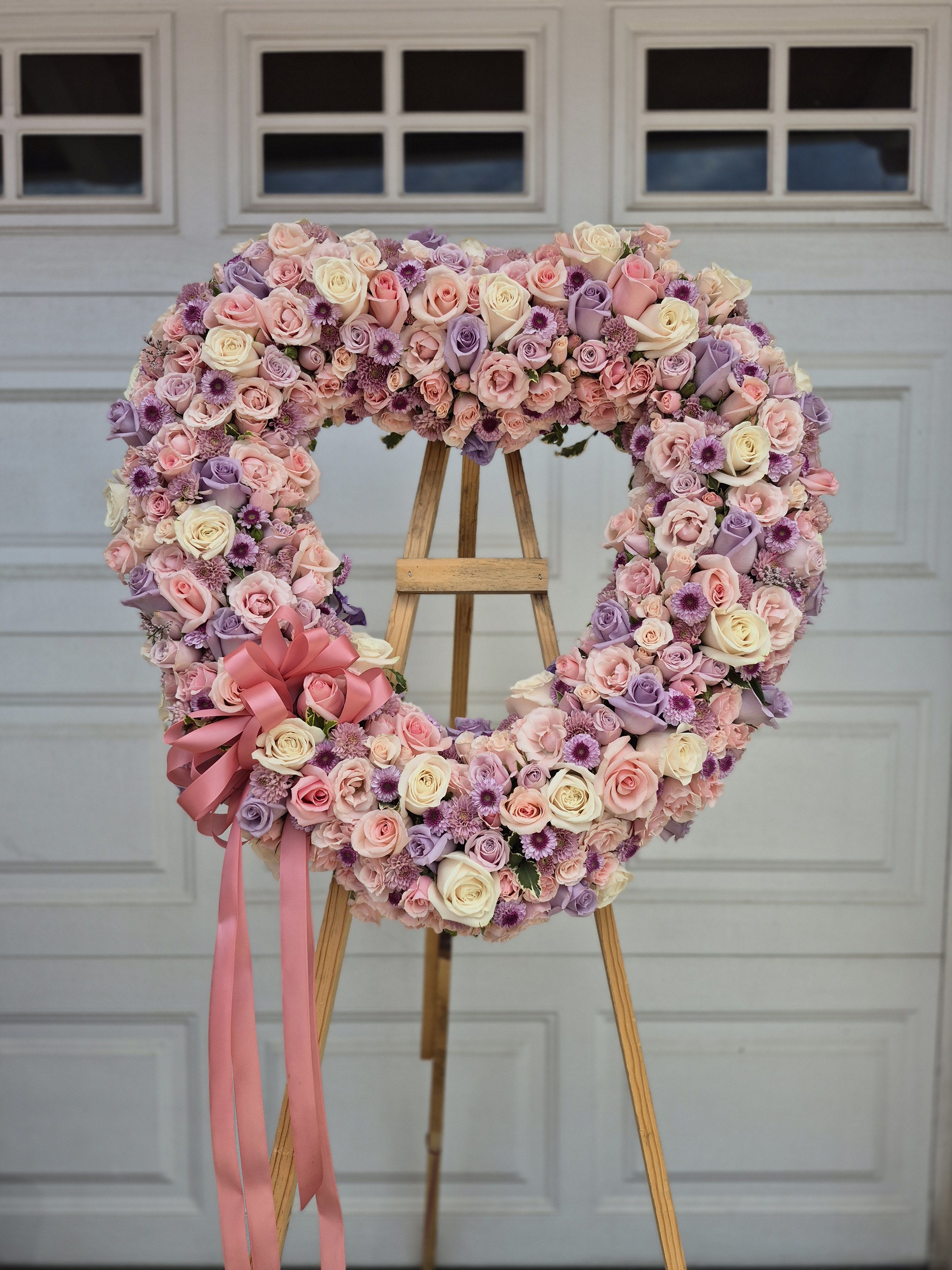 Heart-shaped floral wreath of pink, lavender, and cream roses on an easel