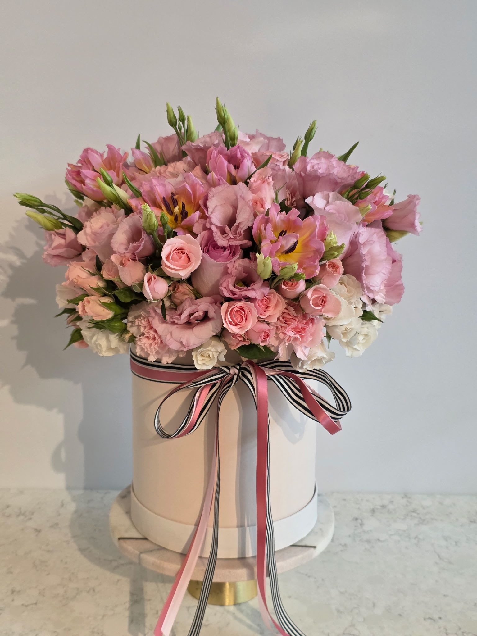 Pink floral arrangement in a round hat box with ribbon bow