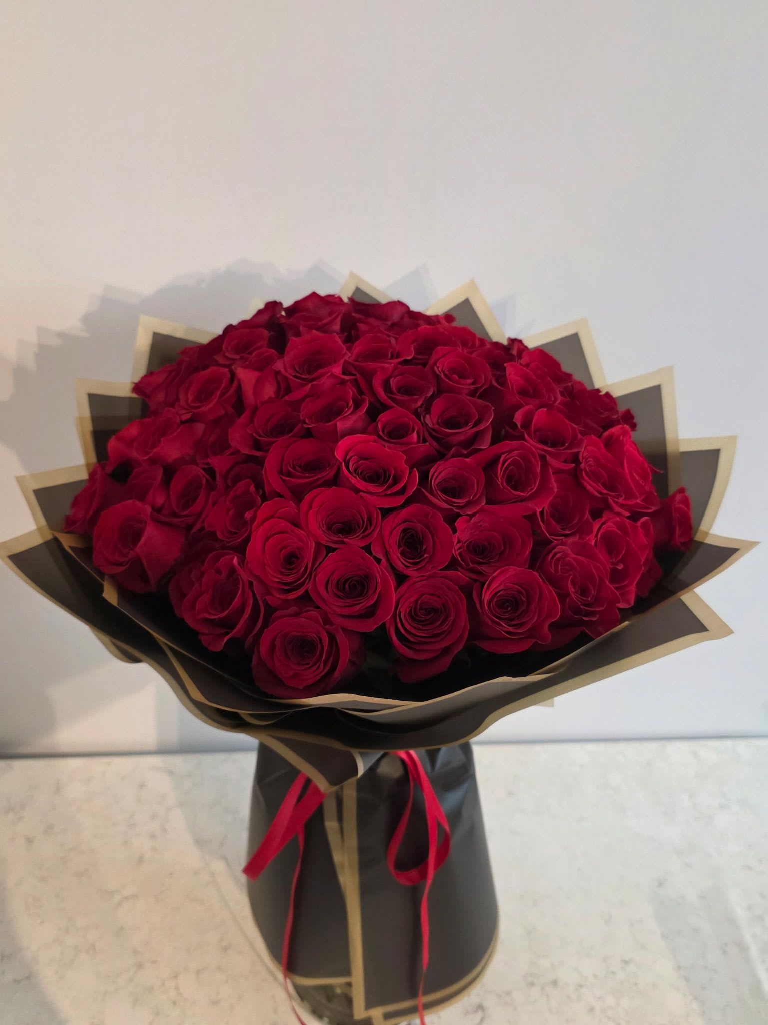 Large bouquet of red roses wrapped in black and gold paper