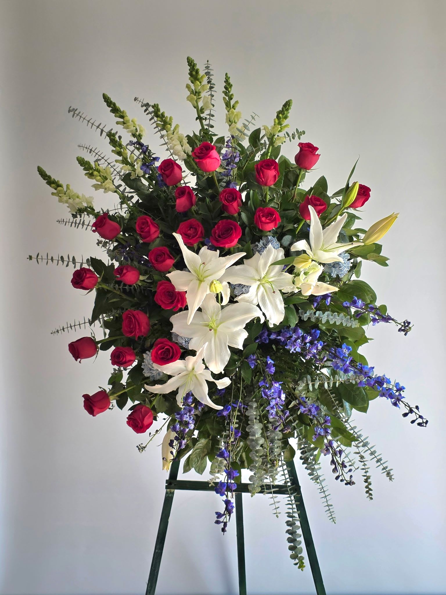 Standing floral spray with red roses, white lilies, and blue flowers