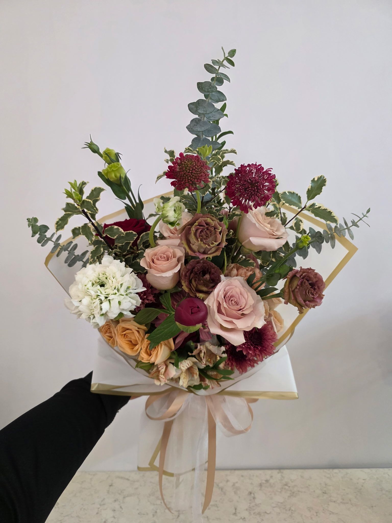 Mixed bouquet of roses and other blooms wrapped in paper with a ribbon