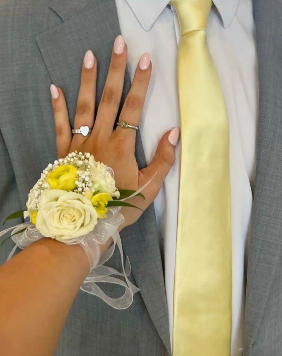 Light Yellow Corsage and Boutonierre - Prom, Weddings, or Formal - A delicate wrist corsage in soft cream-white roses and bright yellow accent blooms that makes a subtle, coordinated statement for prom, weddings, or other formal occasions. The compact cluster-lifted by tiny white filler flowers and touches of greenery-reads romantic and polished so the person you're honoring will feel effortlessly put-together and celebrated.  This petite arrangement is finished with a sheer ribbon tie and comes on a corsage wristlet designed to sit comfortably on the wrist; the translucent ribbon drapes gently below the hand for an elegant, photo-ready look. Colors are a pastel mix of white, yellow, pale pink hints, and green foliage that pairs beautifully with gray suits, pale yellow ties, or soft-toned dresses.  Ideal for the graduate, prom date, or bride's attendant who prefers refined, understated florals, this corsage sends a message of thoughtful elegance without overwhelming an outfit. Order with sizing and delivery in mind so the wristlet fits the wearer comfortably; keep blooms fresh by storing in a cool place and misting lightly until ready to wear.