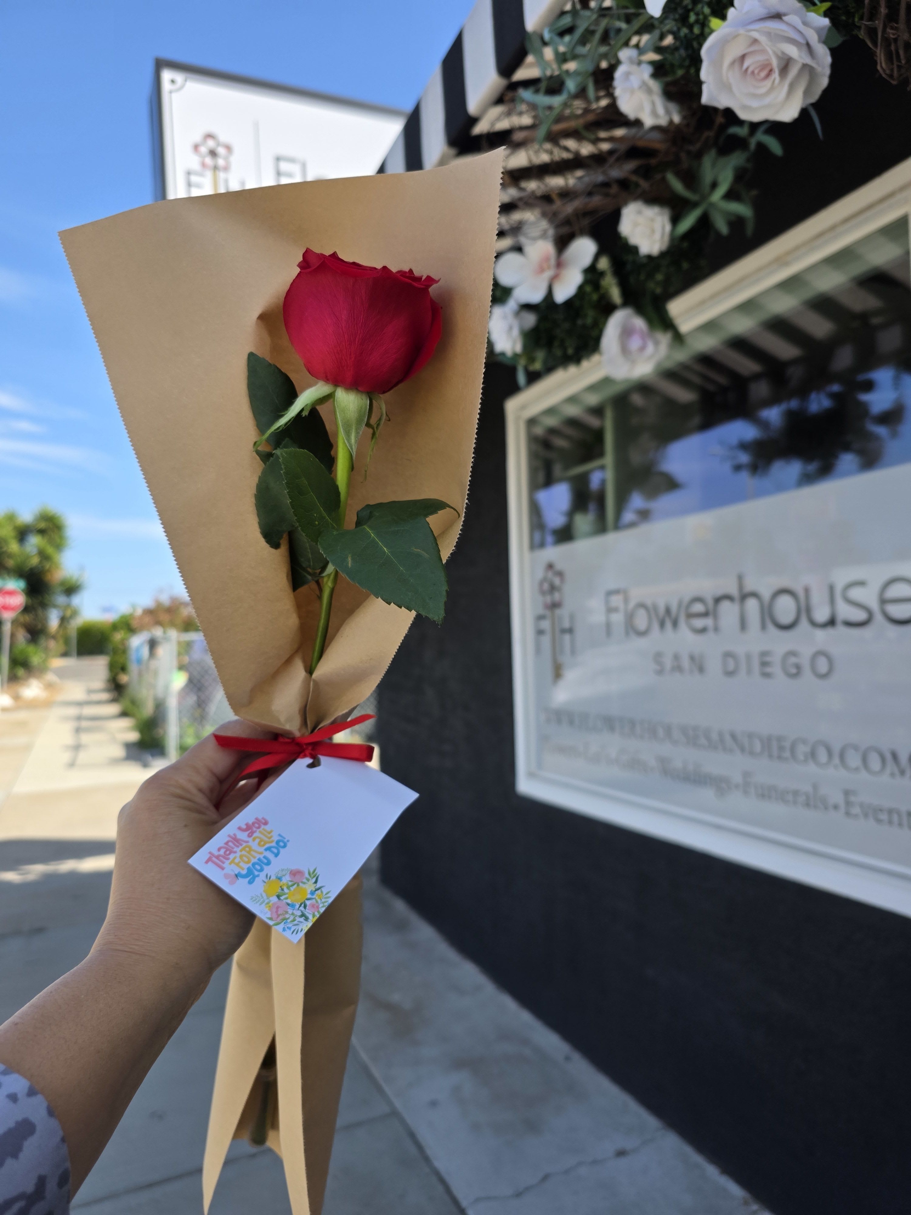 Single Stem Red Roses - Mother's Day - A single long-stem red rose makes a quietly powerful Mother's Day bouquet-a classic red rose arrangement that reads both romantic and deeply grateful. The vivid red bloom sits centered against natural brown paper wrap and a bright red ribbon, the kind of simple, hand-tied presentation that tells the person you're thinking of them in a personal, heartfelt way.  This arrangement features one long-stem red rose with a few dark green leaves, wrapped in rustic brown kraft paper and finished with a red ribbon and gift tag. The contrast of the saturated crimson petals against the neutral wrap creates clean, visual impact and a tactile, handmade feel.  Perfect for a mom who prefers elegance without fuss-use this as a thank-you, Mother's Day surprise, or a small but meaningful love gesture. Easy to care for: place the stem in fresh water upon arrival and remove any leaves below the waterline to keep the single bloom looking its best.