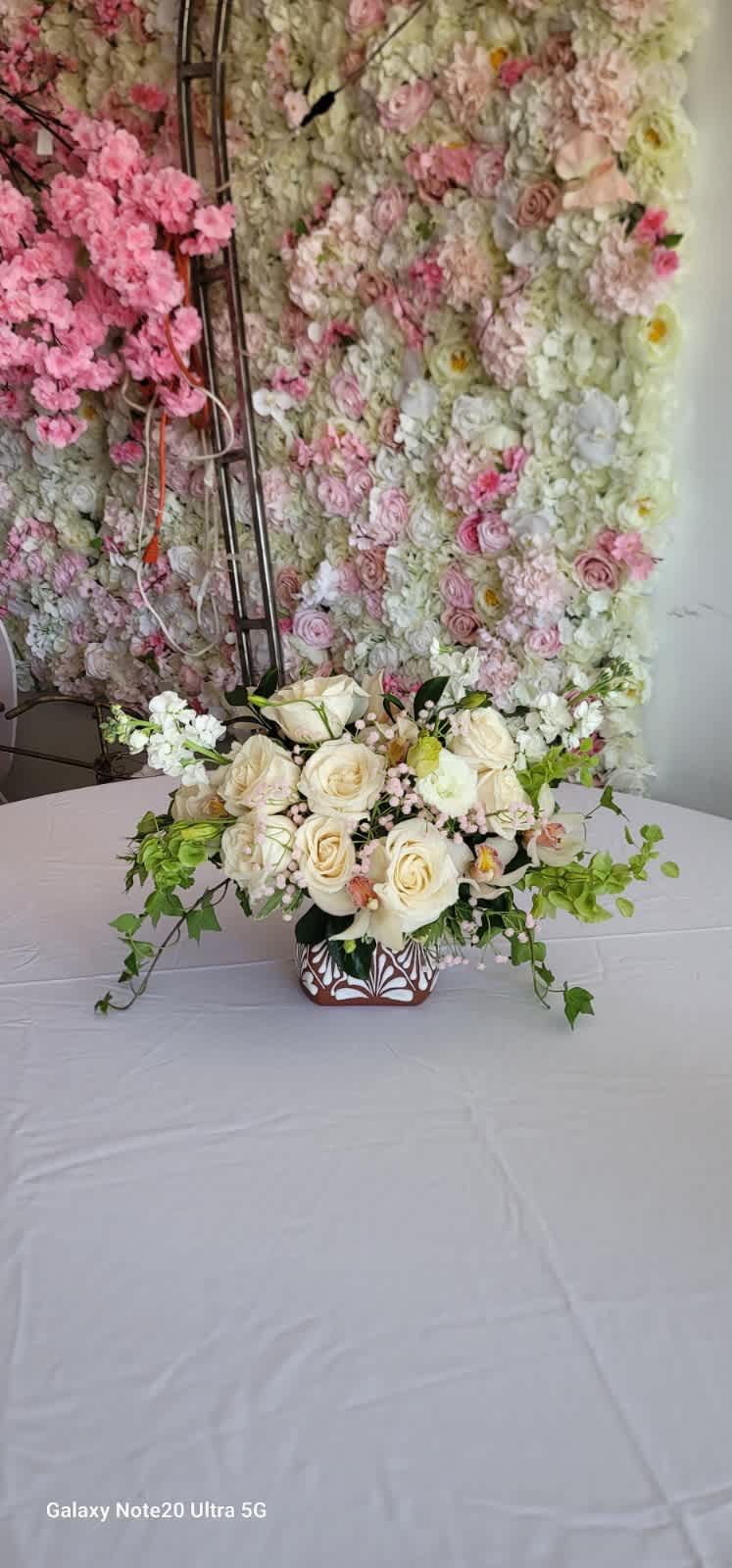Cream rose arrangement in a patterned vase with trailing greenery