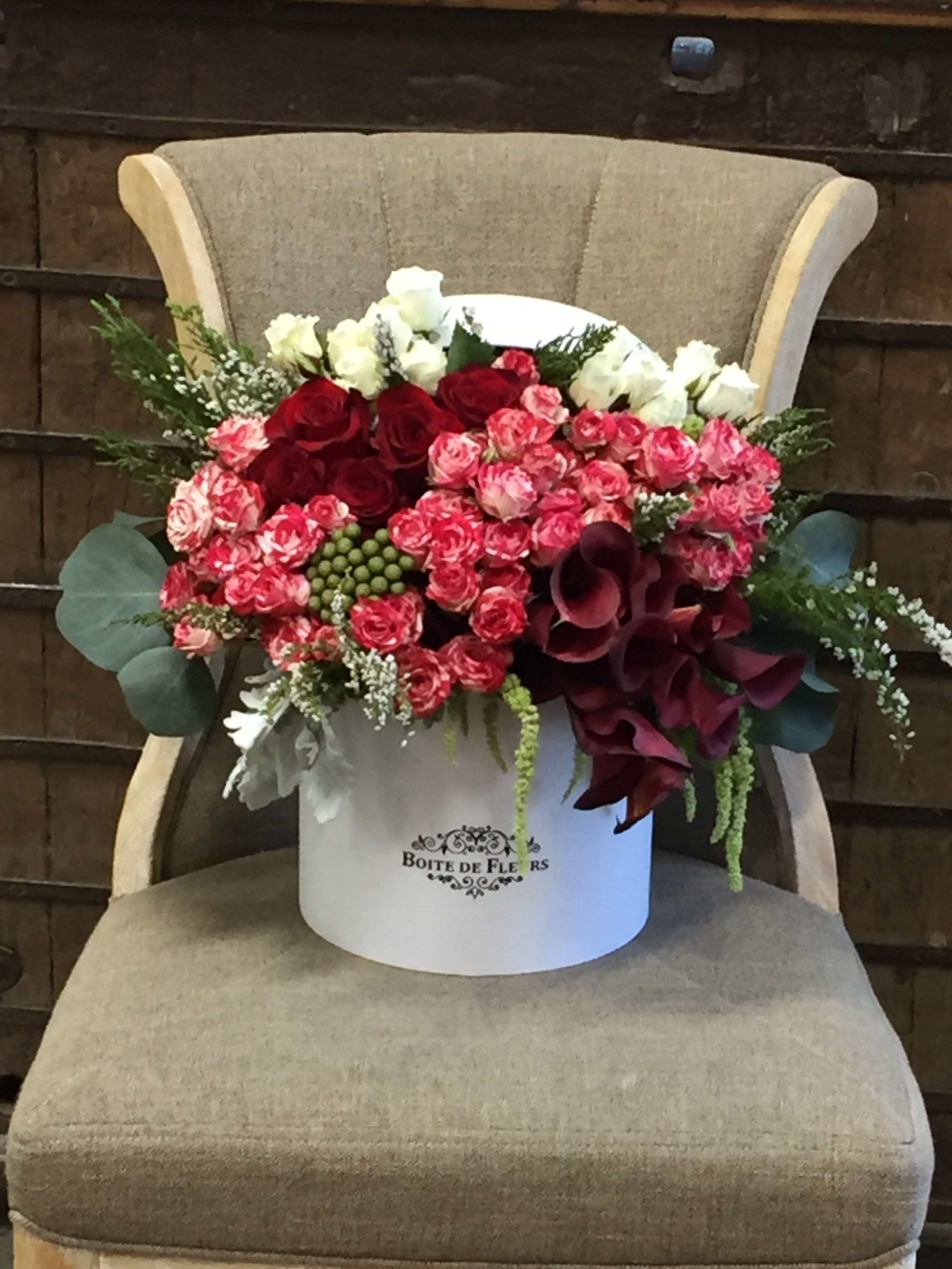 Bouquet of red and pink roses with white blooms in a white hatbox