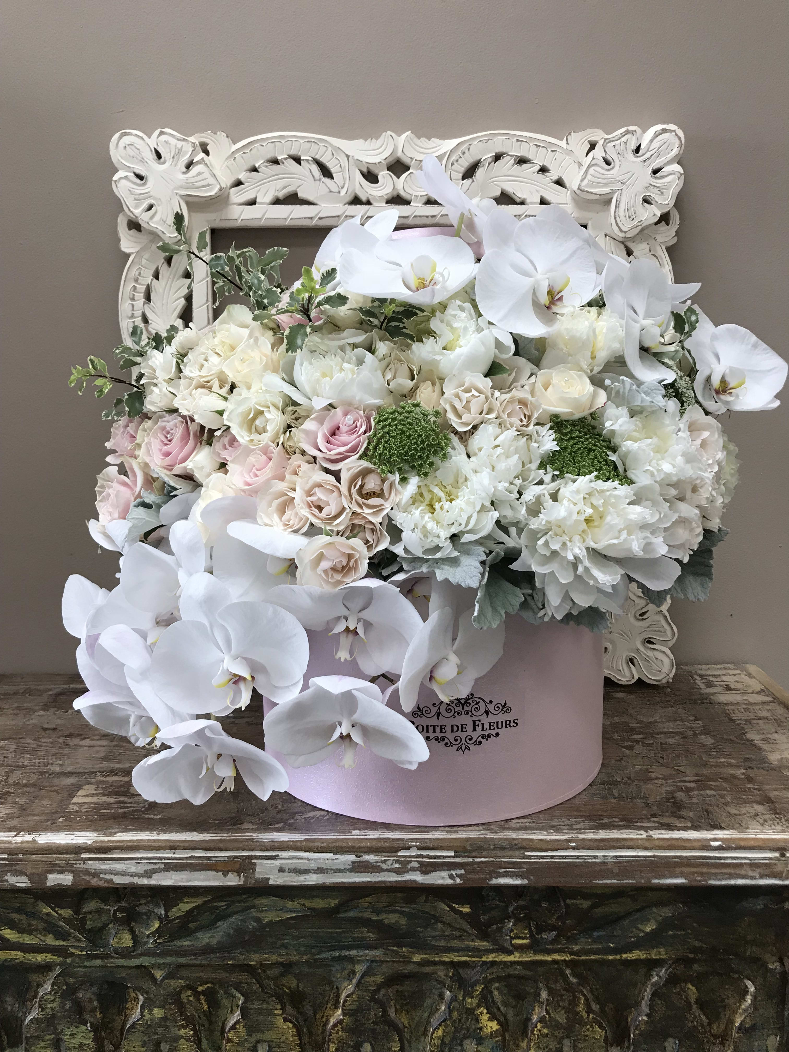 White orchids and pastel roses in a pink hatbox